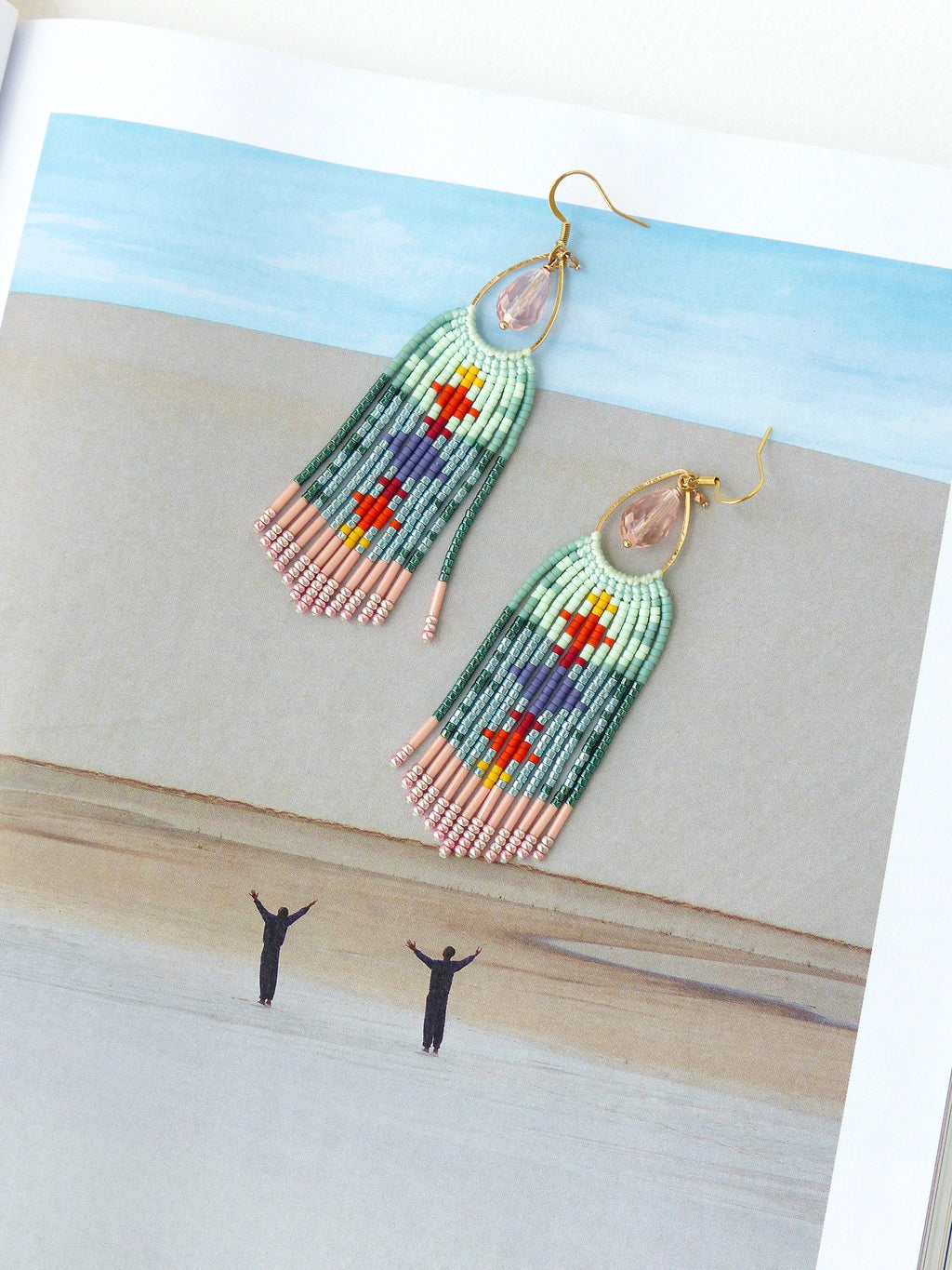 Peut inclure: Une paire de boucles d'oreilles en perles avec un motif géométrique coloré. Les boucles d'oreilles comportent un crochet doré et une perle rose en forme de goutte. Le corps principal des boucles d'oreilles est rectangulaire avec une frange de perles roses en bas.