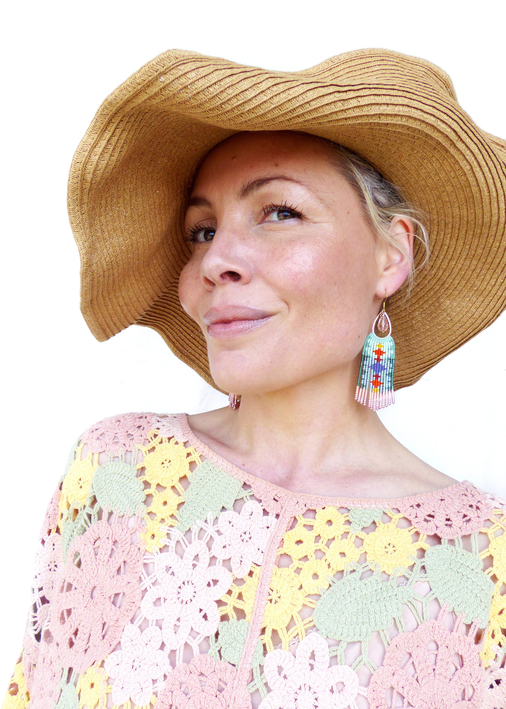 Peut inclure: Boucles d'oreilles en perles avec un motif turquoise, rouge et rose. La personne porte un chapeau de paille et un haut en crochet rose, jaune et vert. Les boucles d'oreilles ont une forme de goutte d'eau avec des franges.
