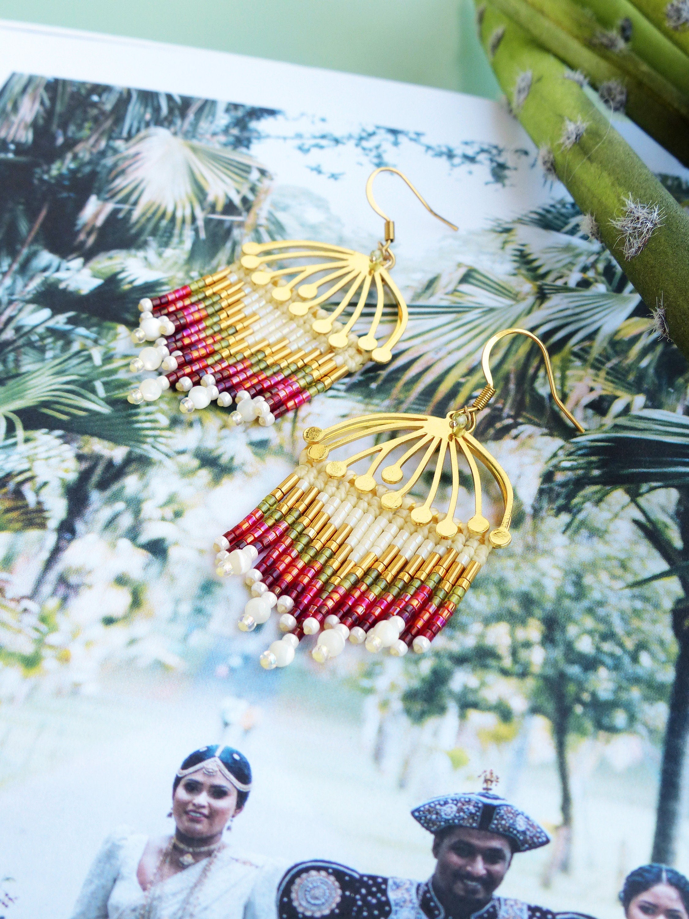 Peut inclure: Boucles d'oreilles dorées avec un motif en forme d'éventail et une frange de perles. Les perles sont dans des tons de rouge, vert, or et blanc.