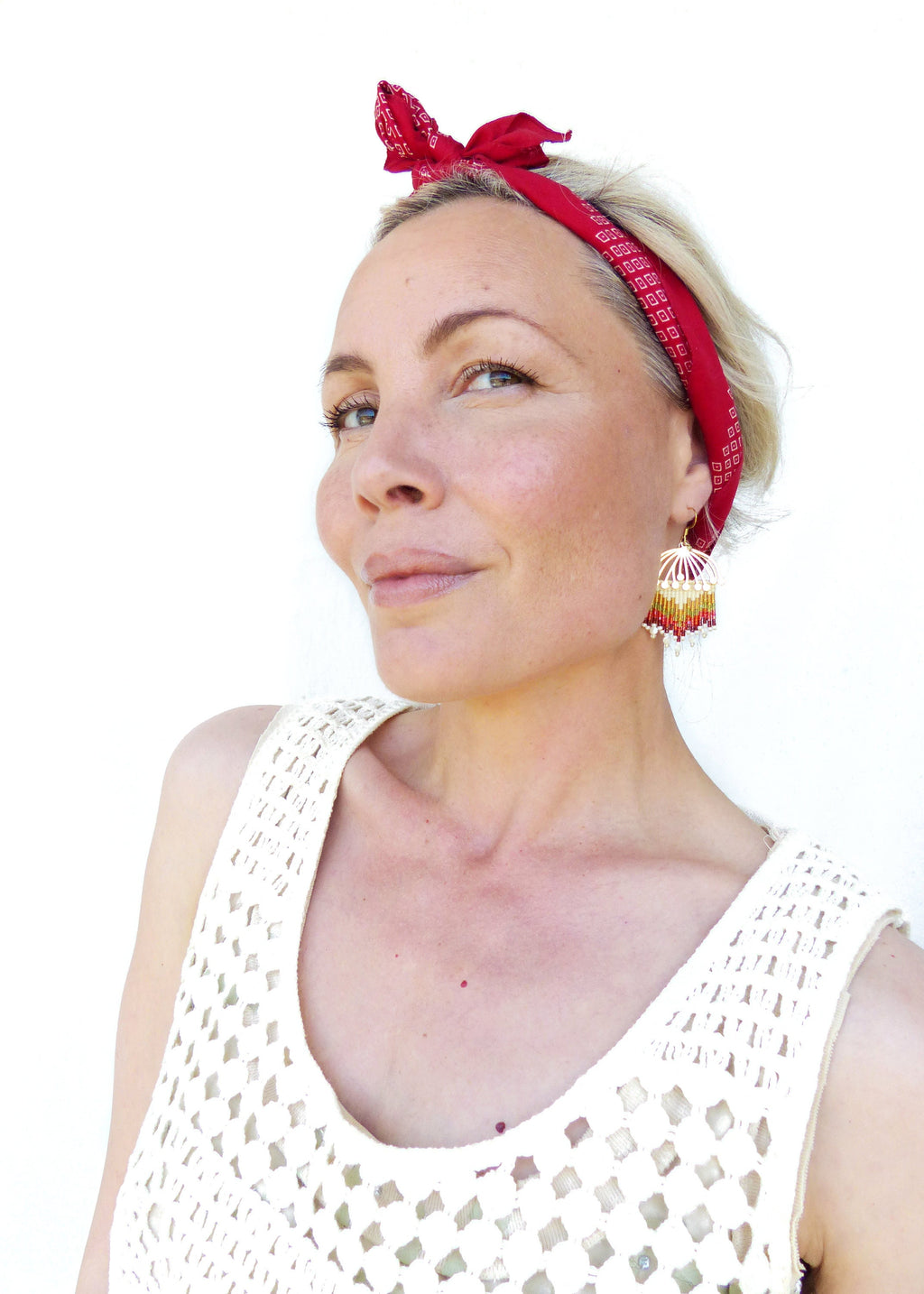 Peut inclure: Une femme aux cheveux blonds portant un bandana rouge et un débardeur en crochet blanc avec des boucles d'oreilles en perles. 