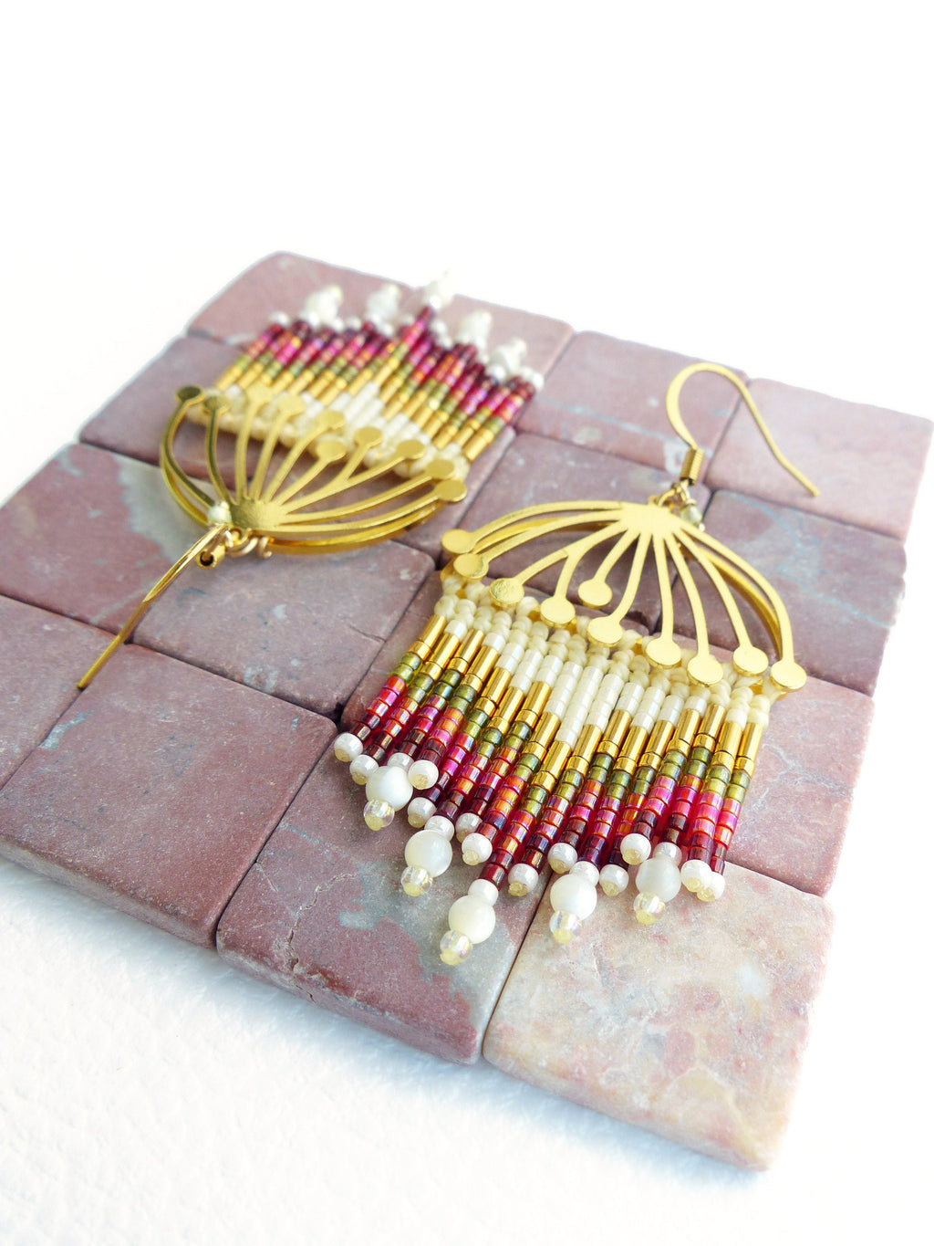 Peut inclure: Une paire de boucles d'oreilles pendantes dorées avec un motif en éventail et une frange de perles rouges, blanches et dorées.
