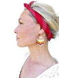 Peut inclure: Une femme portant un bandana rouge à motif géométrique et une paire de boucles d'oreilles en perles dorées et multicolores. Les boucles d'oreilles sont longues et pendantes, avec une forme de larme.