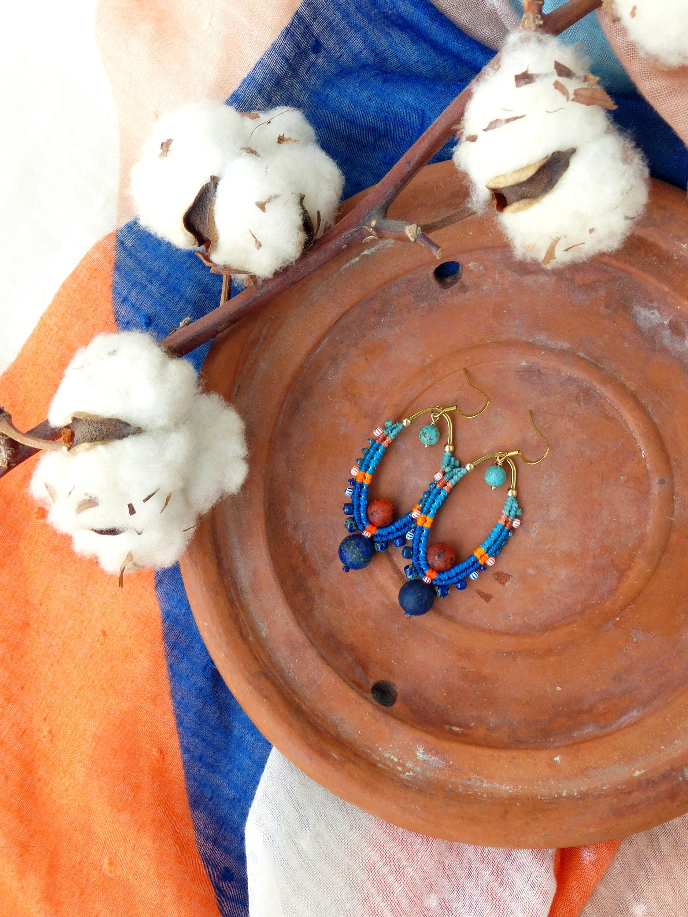 Peut inclure: Une paire de boucles d'oreilles faites à la main avec des perles bleues, orange et turquoise, et des accents dorés. Les boucles d'oreilles sont présentées sur une assiette en terre cuite.