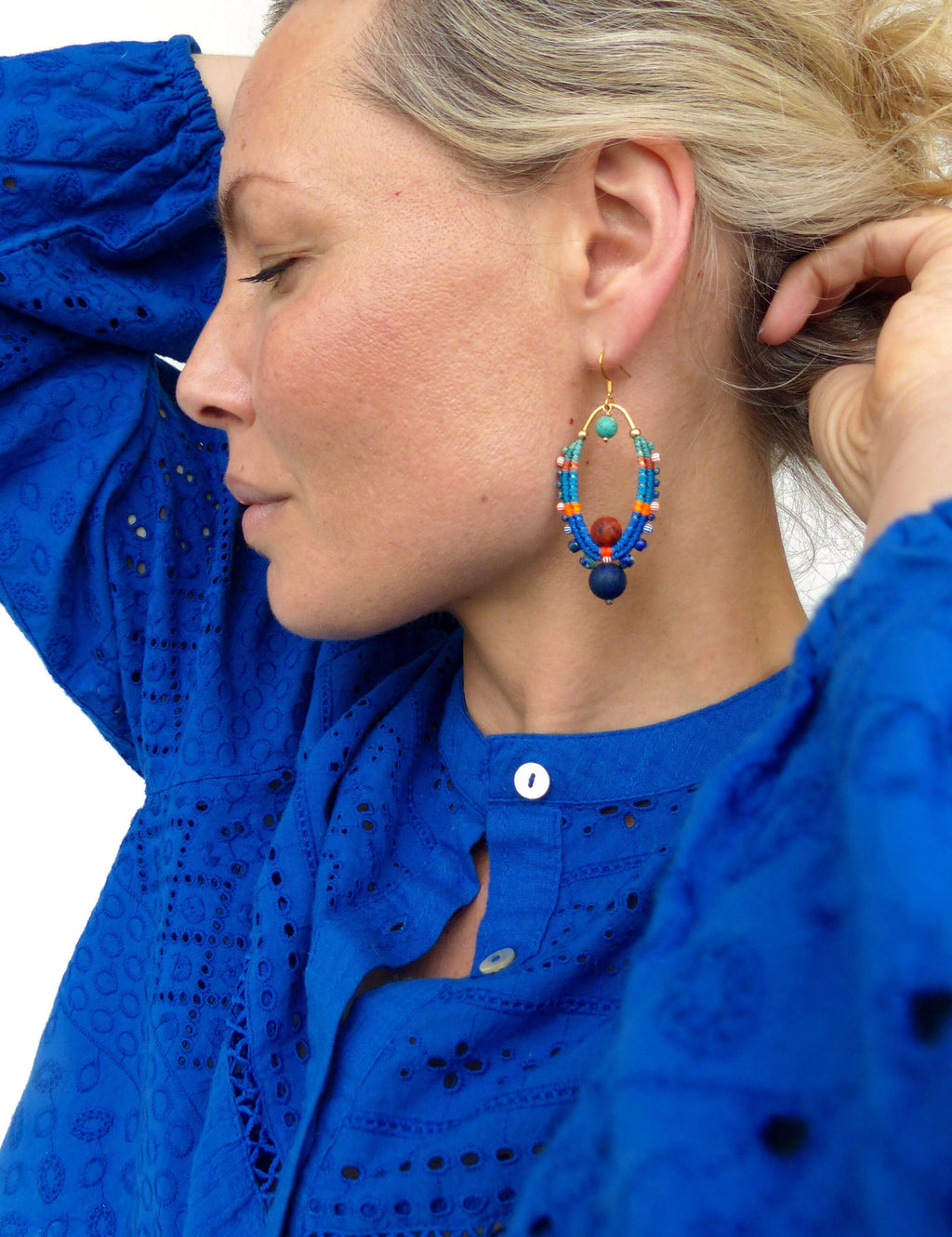 Peut inclure: Une femme portant une chemise bleue brodée avec une paire de boucles d'oreilles en forme d'ovale. Les boucles d'oreilles sont faites de perles bleues, orange, rouges et turquoise.