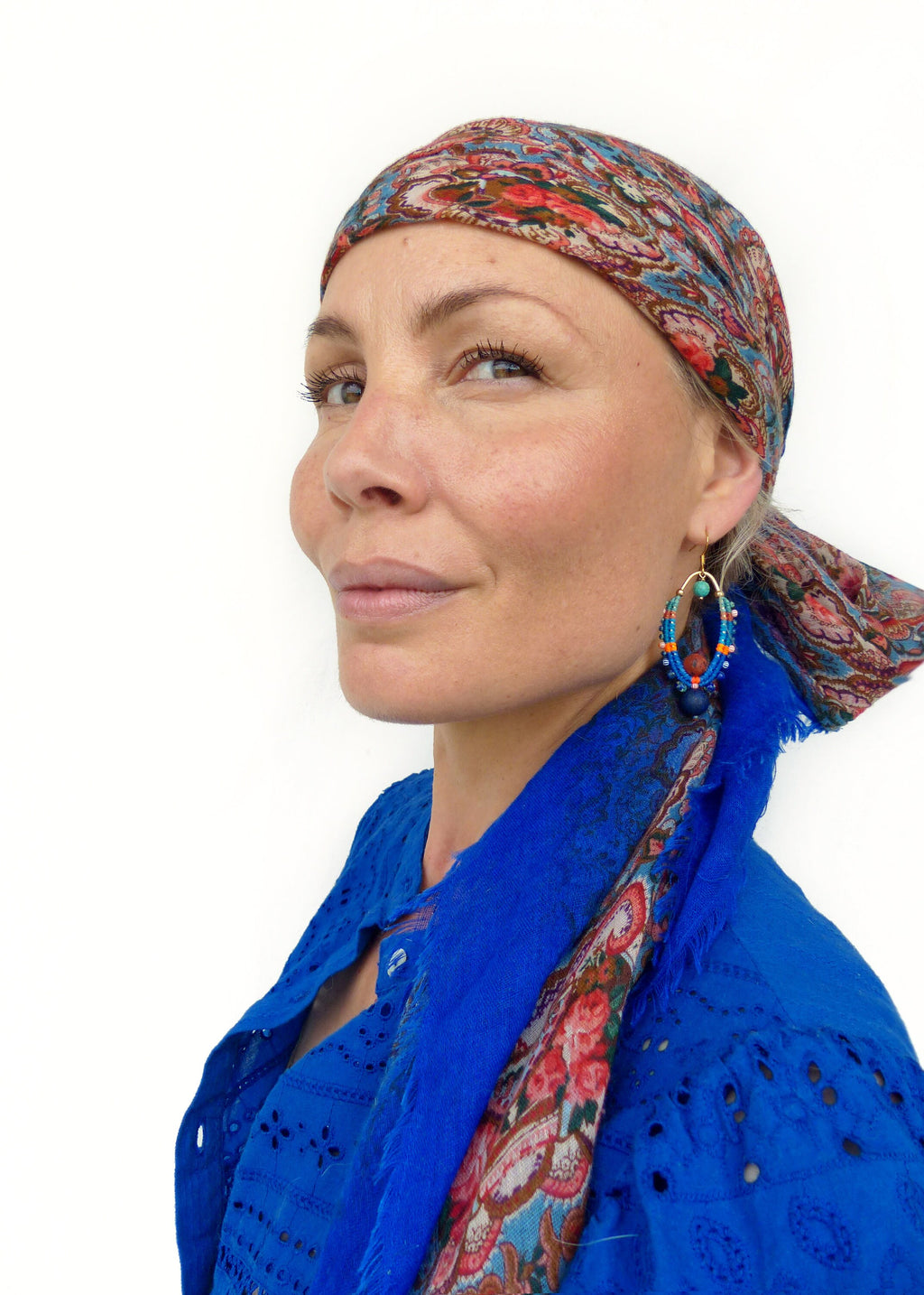 Peut inclure: Une femme portant une chemise bleue avec un foulard à motifs floraux noué autour de la tête. Elle porte une paire de boucles d'oreilles en perles bleues et dorées.