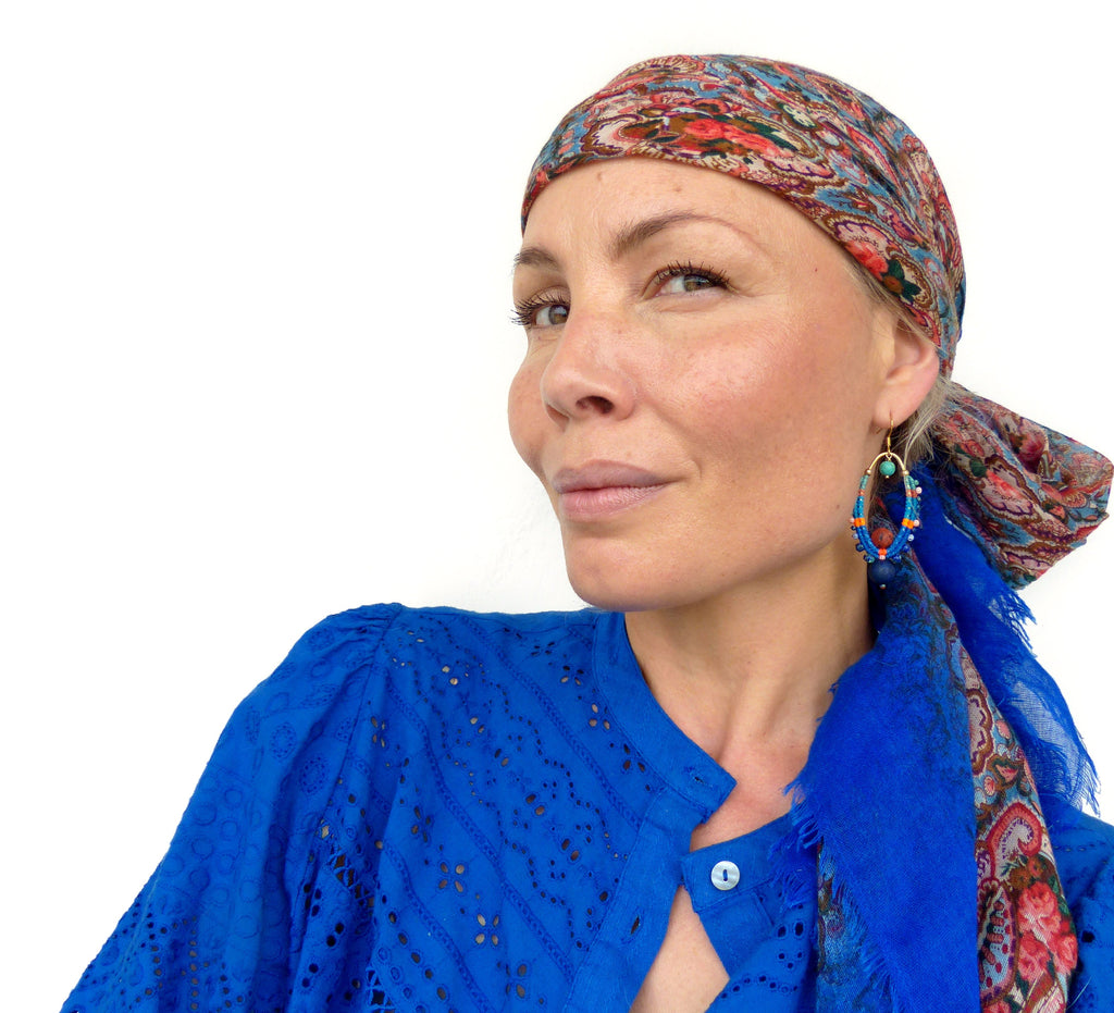 Peut inclure: Une femme portant un foulard à motifs bleus et des boucles d'oreilles bleues porte une blouse bleue à manches longues et en dentelle.