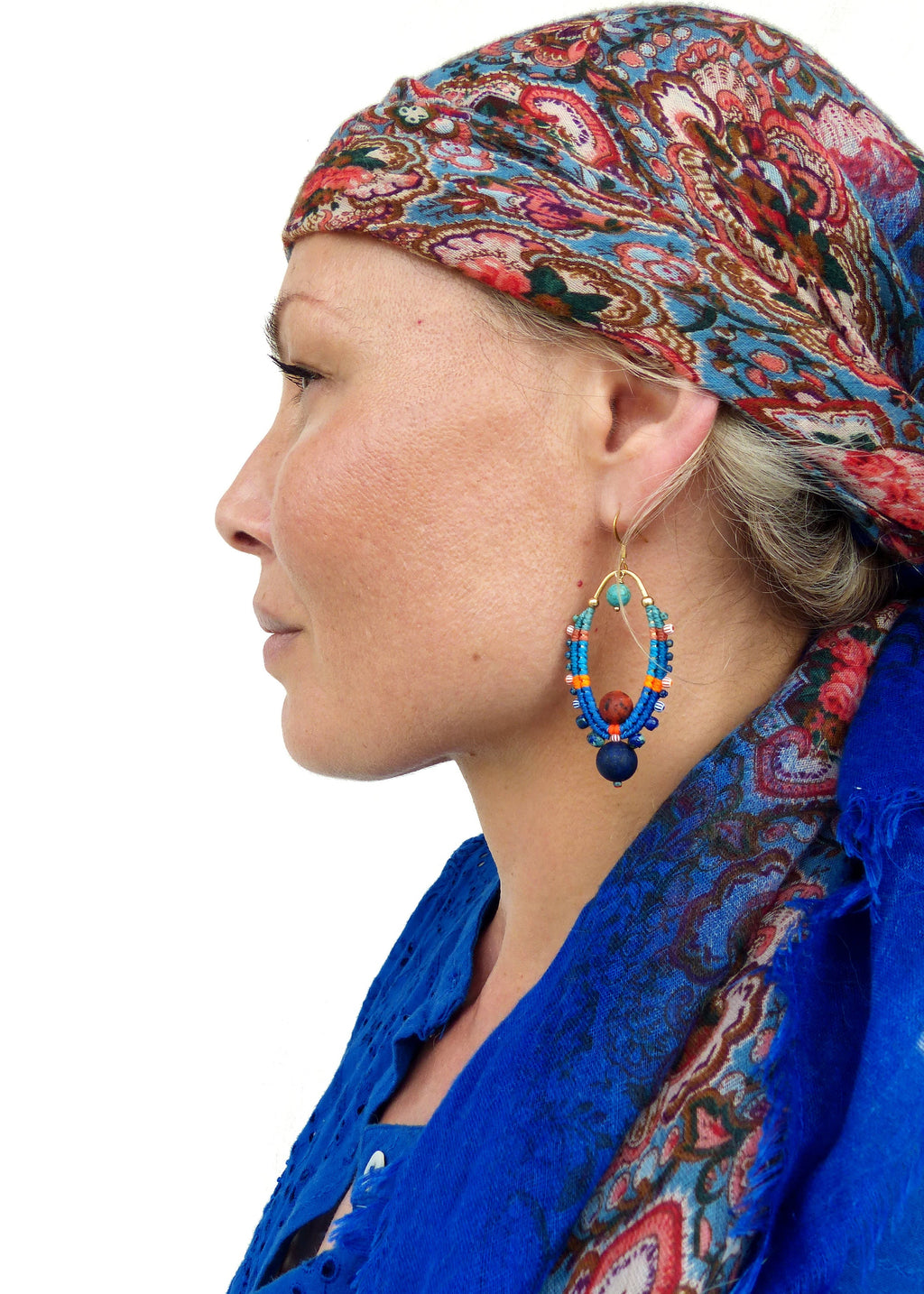 Peut inclure: Une femme portant un foulard à motifs bleus et une chemise bleue avec une paire de grandes boucles d'oreilles ovales avec des perles bleues, orange et brunes.