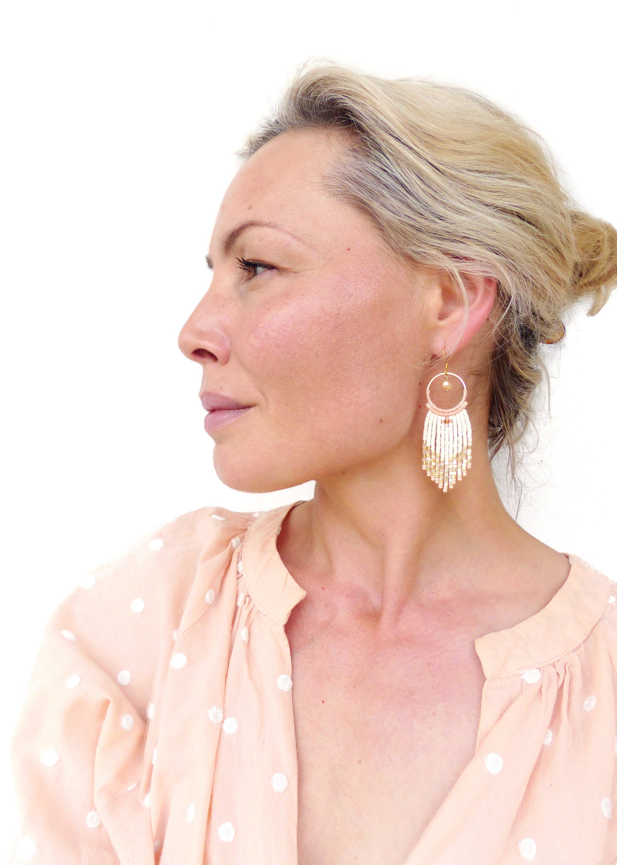 Peut inclure: Une femme portant un chemisier rose à pois blancs avec des boucles d'oreilles en perles blanches. Les boucles d'oreilles sont dorées et blanches avec un motif circulaire.