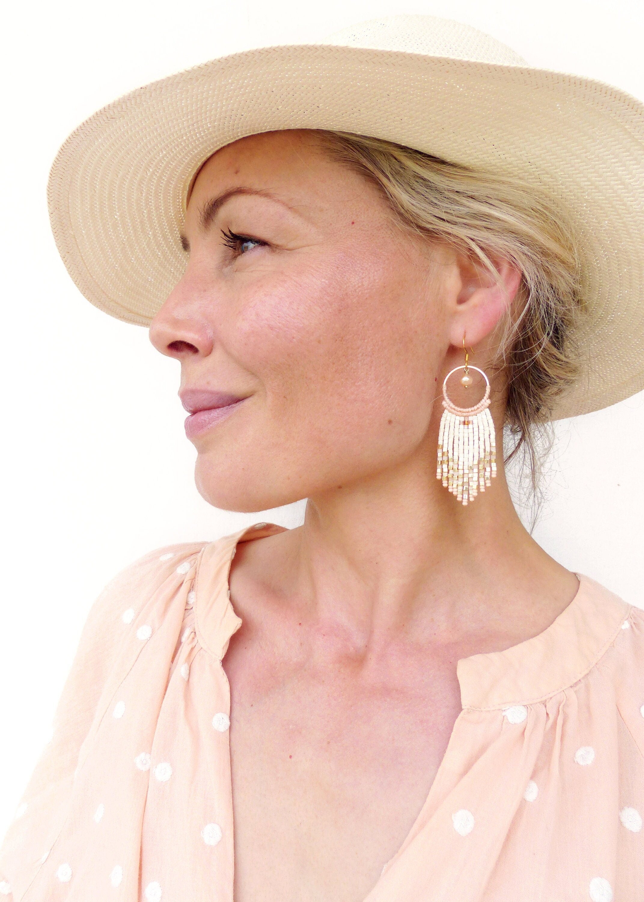 Peut inclure: Une femme portant un chapeau de paille et une blouse pêche à pois blancs. Elle porte de longues boucles d'oreilles en perles blanches et dorées avec un motif circulaire.