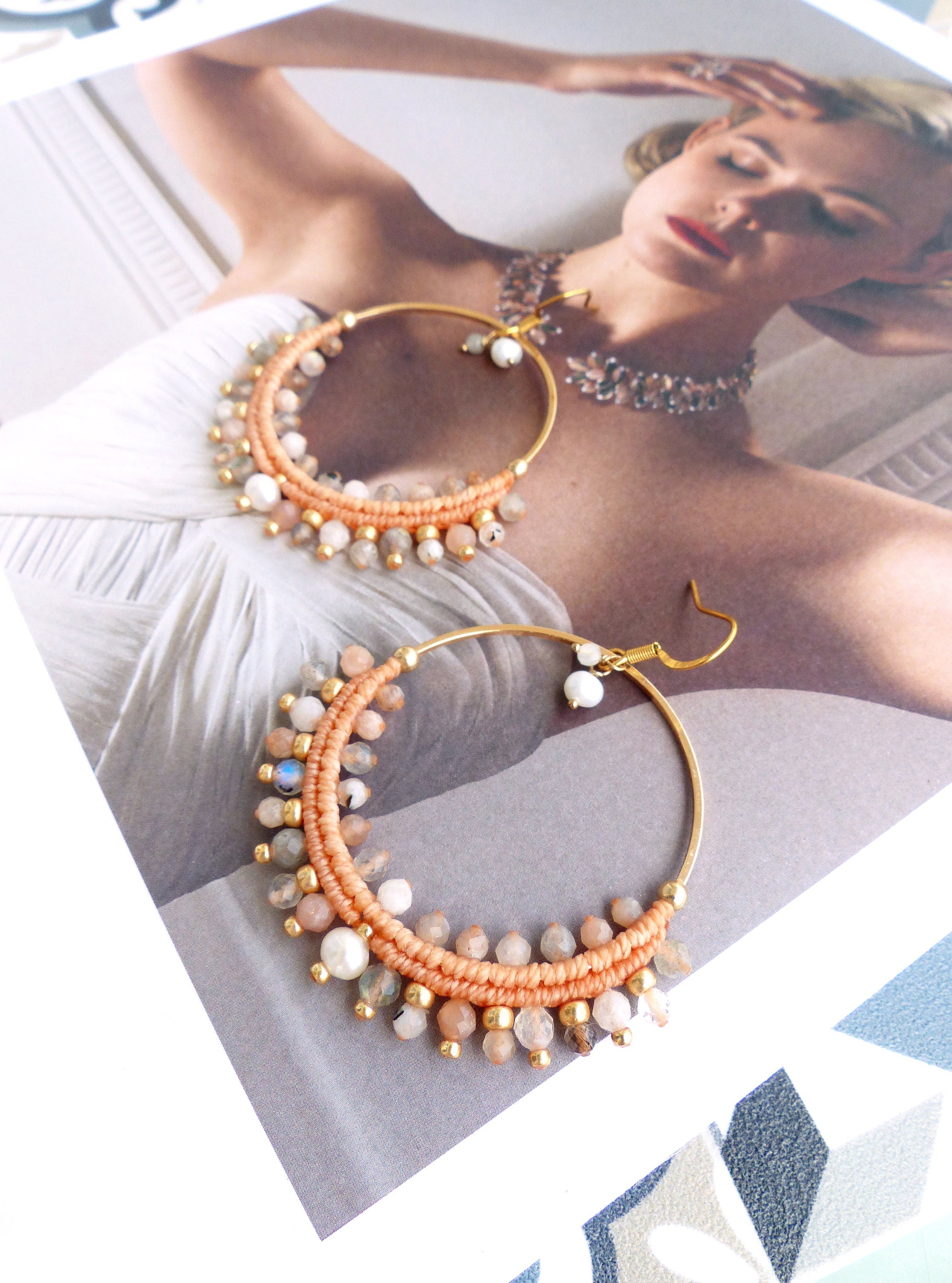 Peut inclure: Une paire de boucles d'oreilles créoles dorées avec du fil de couleur pêche et une variété de pierres claires, dont de la pierre de lune et des perles.