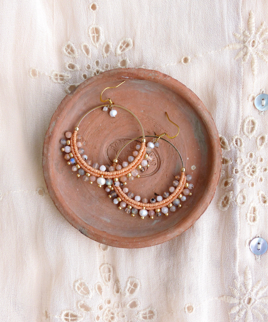 Peut inclure: Une paire de boucles d'oreilles créoles de couleur pêche avec un fil d'or et une variété de petites perles irisées. Les boucles d'oreilles sont présentées sur une assiette en terre cuite.