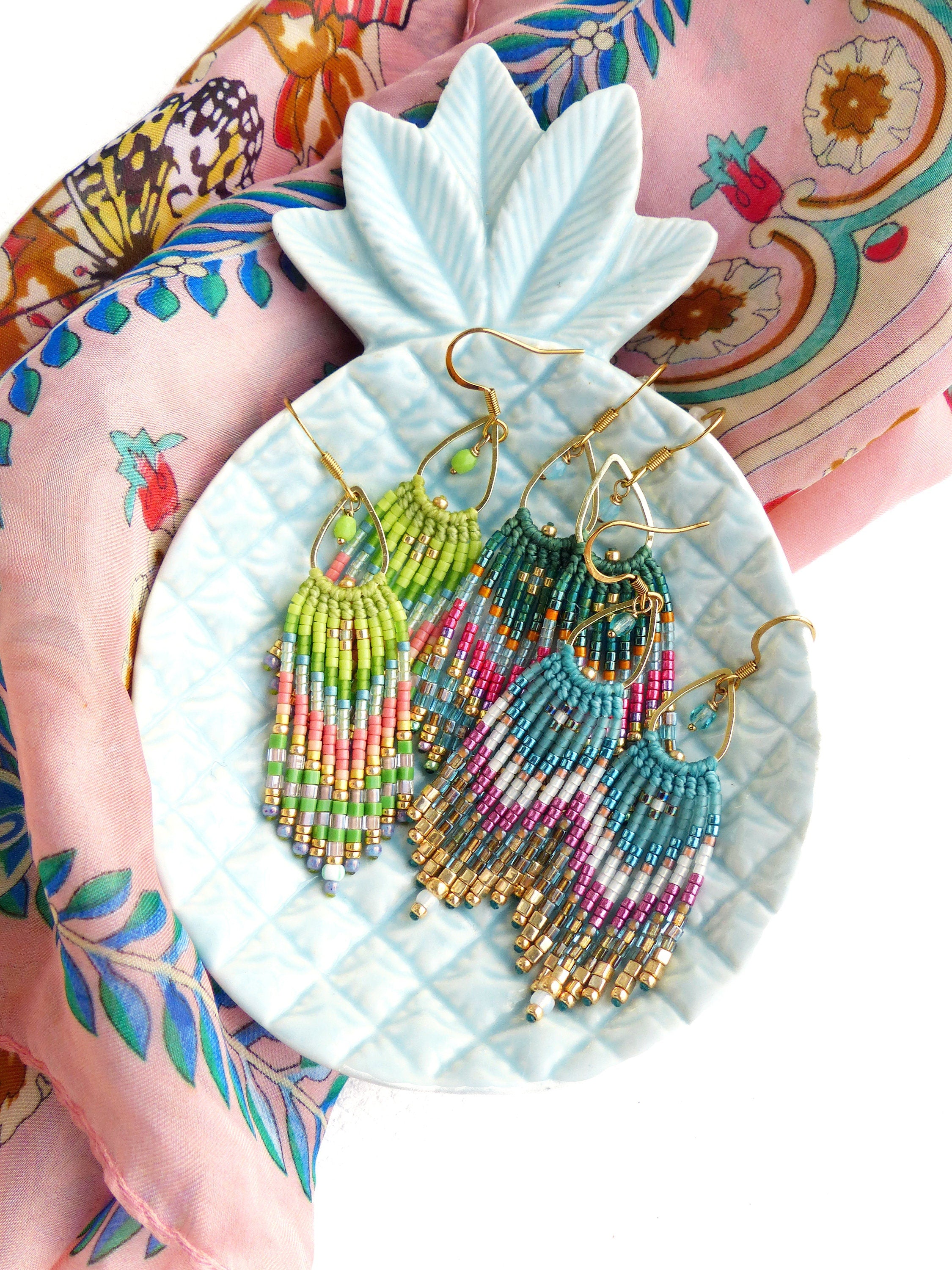 Peut inclure: Trois paires de boucles d'oreilles pendantes en perles colorées avec des crochets dorés, présentées sur un plat en forme d'ananas bleu clair.