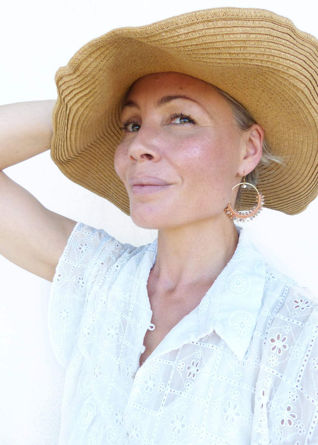 Peut inclure: Une femme portant une blouse blanche brodée avec un chapeau de paille et de grandes boucles d'oreilles en forme de cerceau perlé. Les boucles d'oreilles sont faites de matériaux naturels et ont une couleur brun clair.