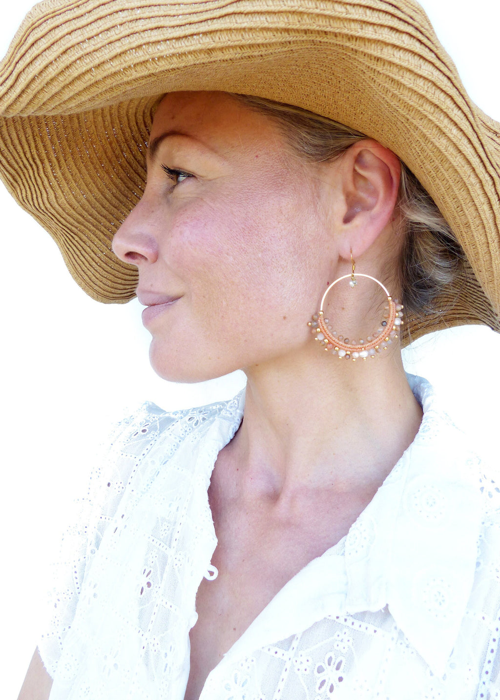 Peut inclure: Une femme portant un chapeau de paille à larges bords et une blouse en dentelle blanche avec une grande boucle d'oreille en forme de cercle perlé à l'oreille droite. La boucle d'oreille est faite de perles de couleur pêche et a un cadre en fil d'or.