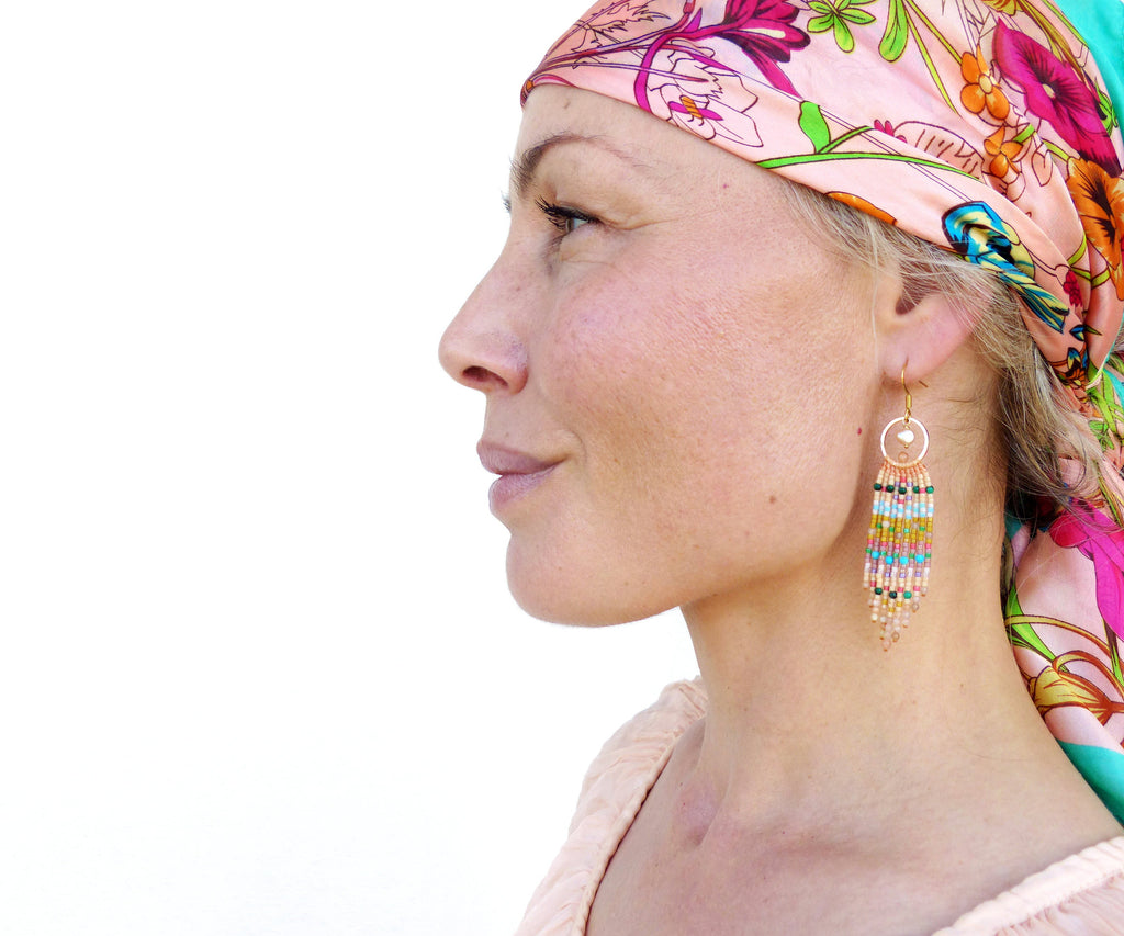 Peut inclure: Une femme portant un foulard à motifs floraux et des boucles d'oreilles en perles. Les boucles d'oreilles sont longues et pendantes, avec une variété de couleurs, notamment le rose, le bleu, le vert et l'or.
