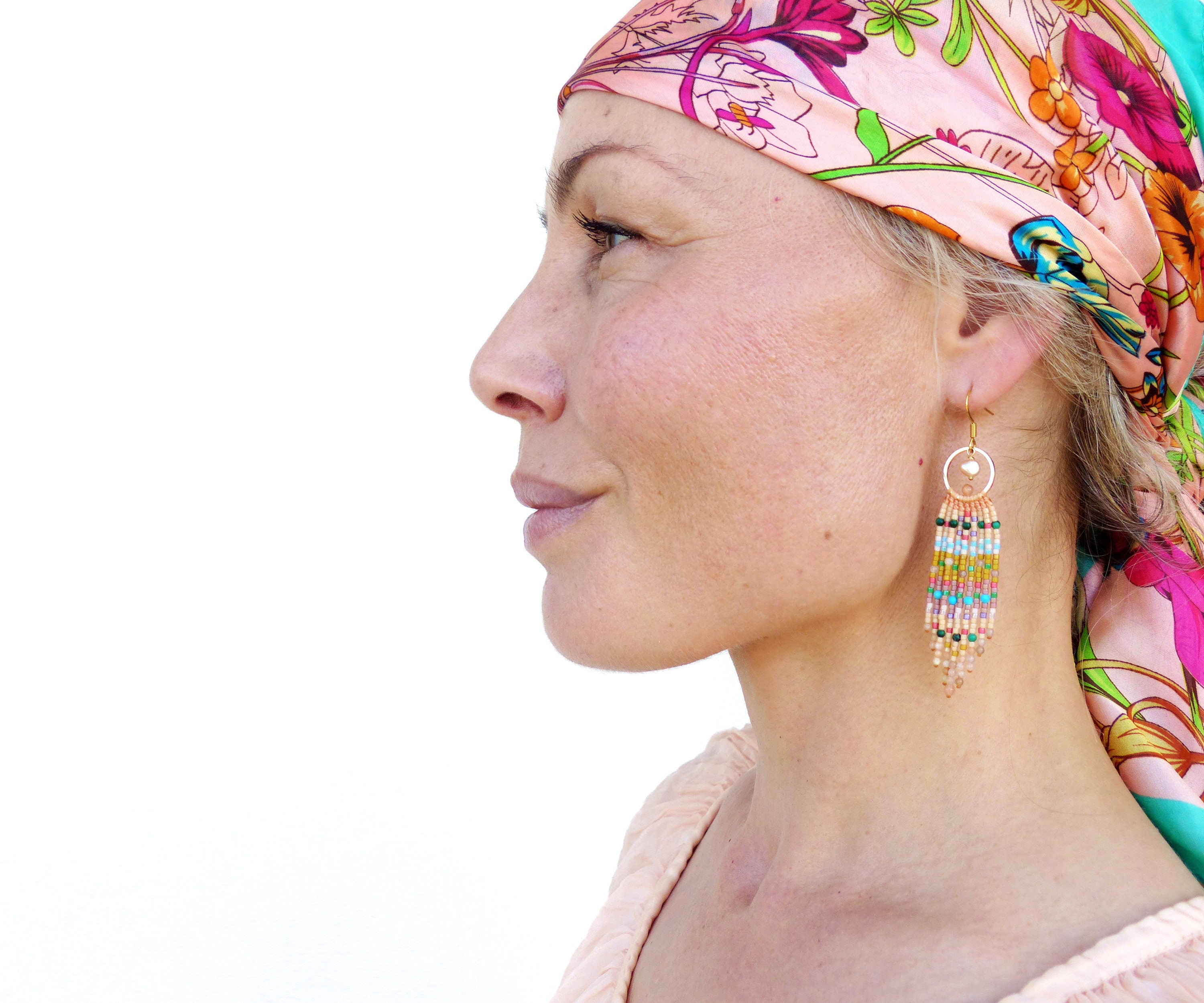 Peut inclure: Une femme portant un foulard à motifs floraux et des boucles d'oreilles en perles. Les boucles d'oreilles sont longues et pendantes, avec une variété de couleurs, notamment le rose, le bleu, le vert et l'or.