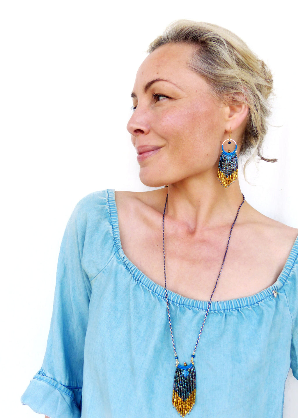Peut inclure: Une femme portant un haut bleu clair à épaules dénudées avec un collier et des boucles d'oreilles en perles. Le collier et les boucles d'oreilles sont faits de perles bleues, dorées et argentées.