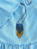 Peut inclure: Un collier de perles bleu et or avec un pendentif en frange. Le collier est sur un fond en jean bleu.