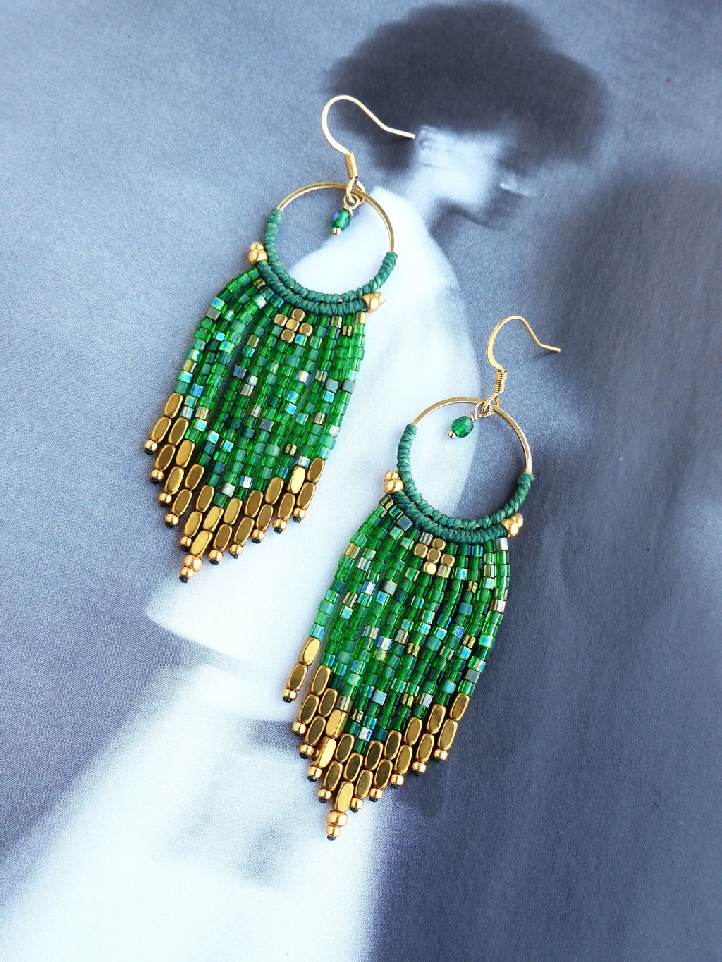 Peut inclure: Une paire de boucles d'oreilles pendantes en perles vertes et dorées. Les boucles d'oreilles sont faites de petites perles carrées et de perles dorées. Les boucles d'oreilles mesurent environ 7,5 cm de long.