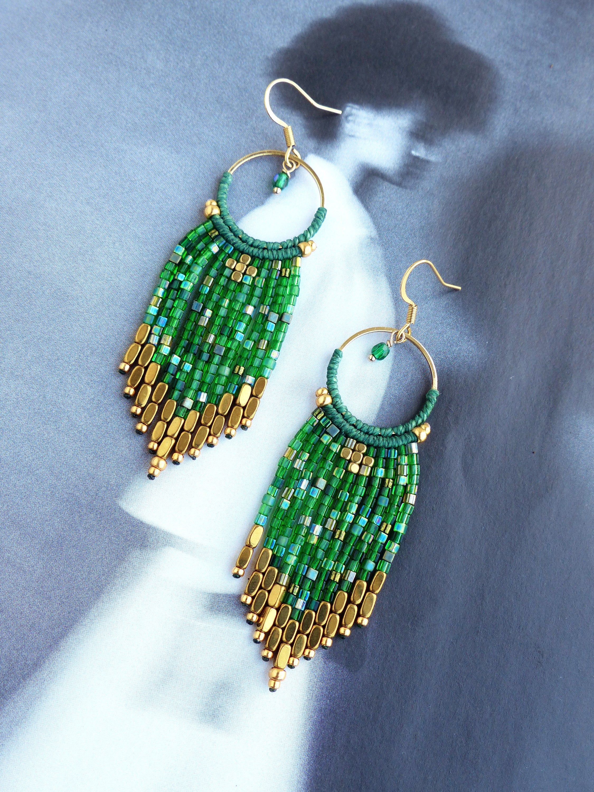 Peut inclure: Une paire de boucles d'oreilles pendantes en perles vertes et dorées. Les boucles d'oreilles sont faites de petites perles carrées et de perles dorées. Les boucles d'oreilles mesurent environ 7,5 cm de long.