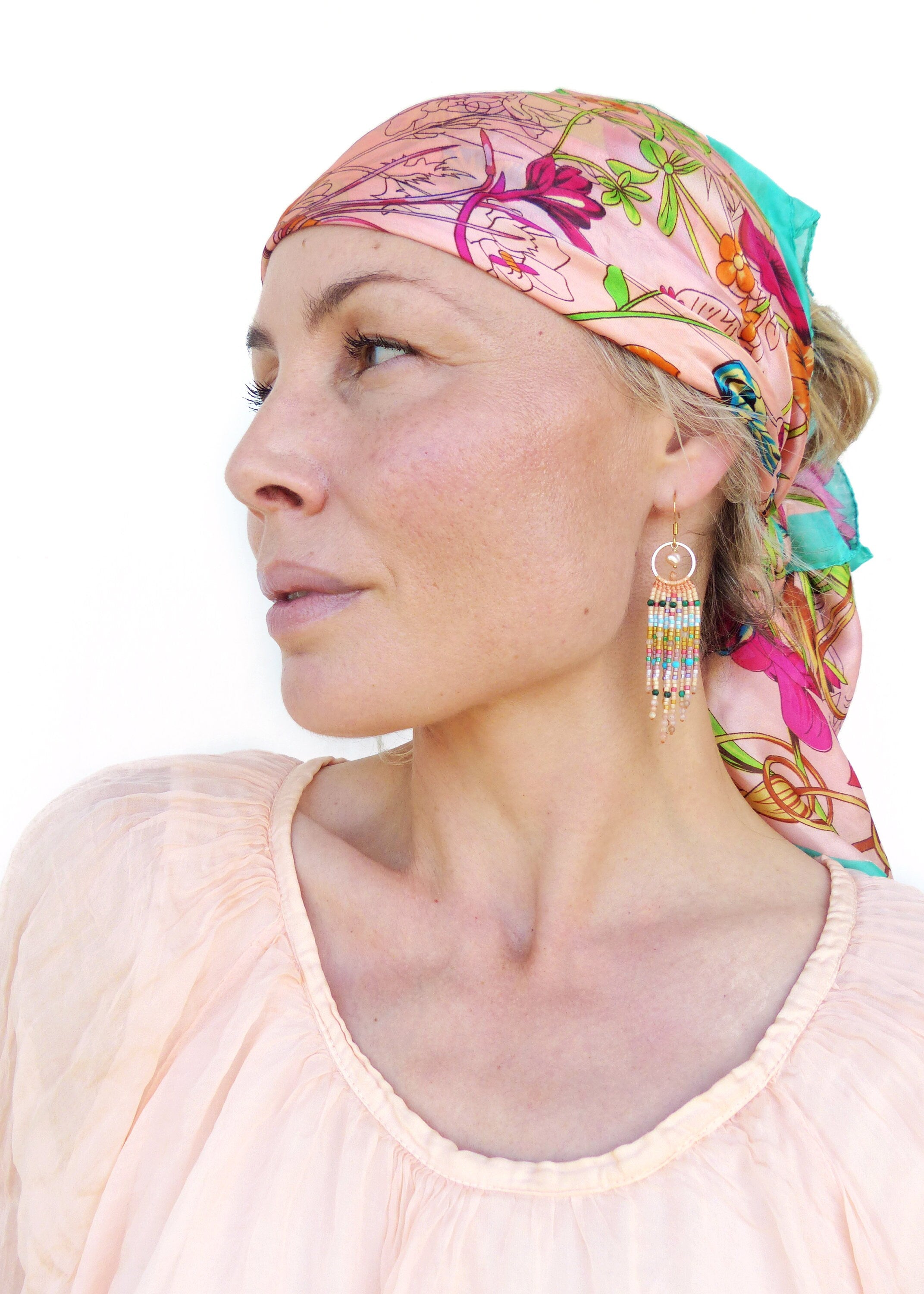 Peut inclure: Une femme portant un foulard floral rose et un chemisier pêche avec des boucles d'oreilles en perles. Les boucles d'oreilles sont longues et pendantes, avec un mélange de perles colorées.