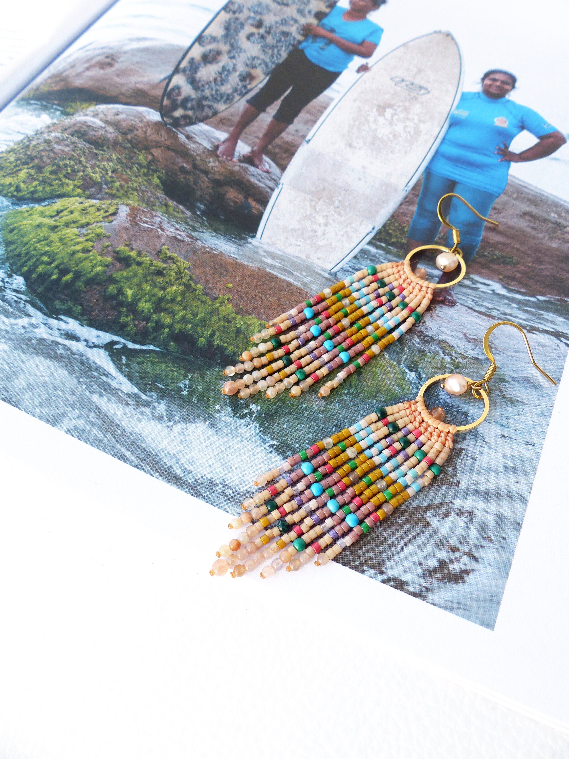 Peut inclure: Une paire de longues boucles d'oreilles en perles colorées avec des cercles dorés et un accent de perle. Les boucles d'oreilles sont faites avec une variété de petites perles dans des tons de brun, rose, jaune, vert, bleu et turquoise.