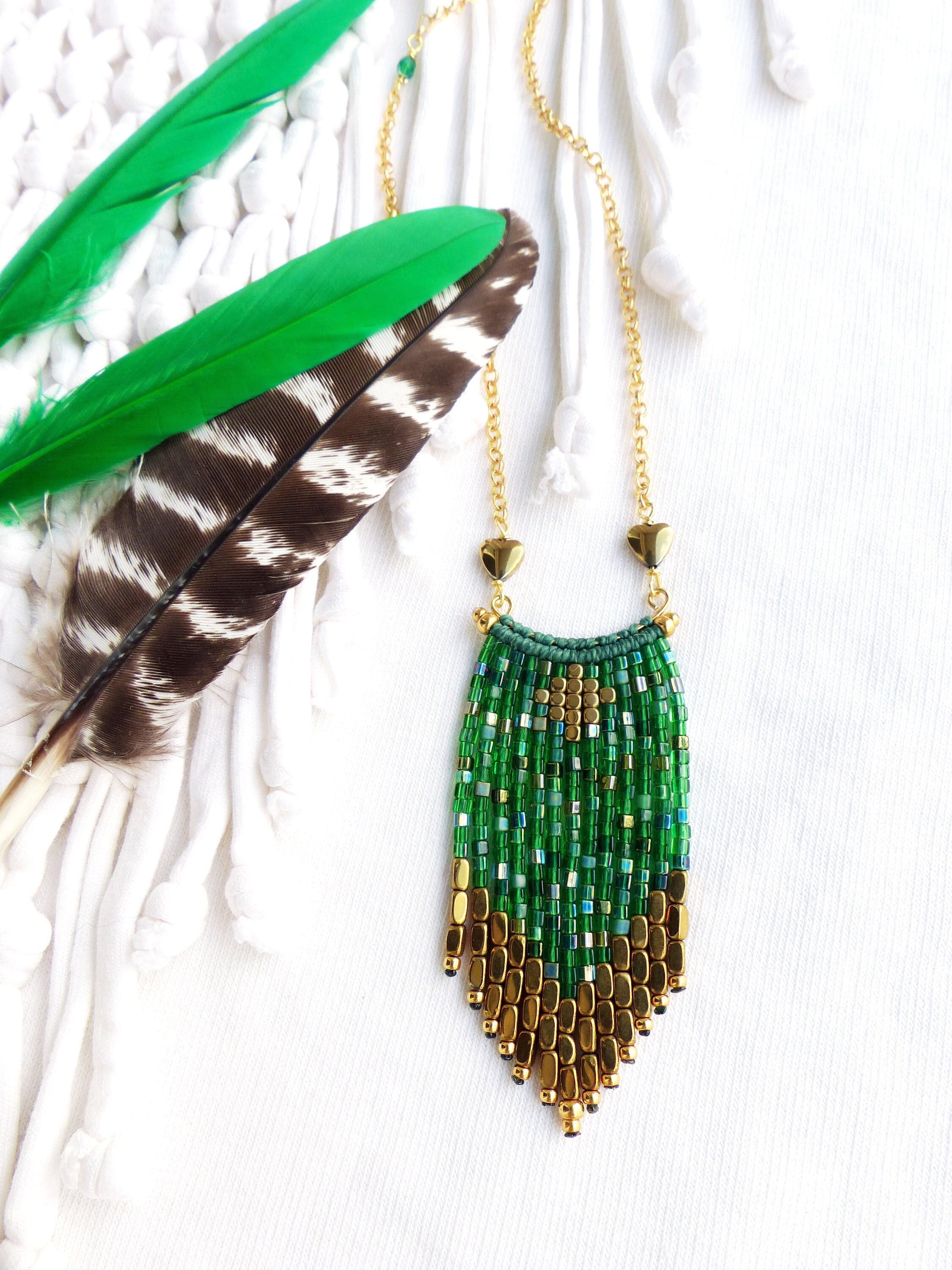 Peut inclure: Un collier en chaîne dorée avec un pendentif en franges de perles vertes et dorées. Le pendentif est composé de petites perles carrées dans des tons de vert et d'or, avec un charme en forme de cœur doré en haut.