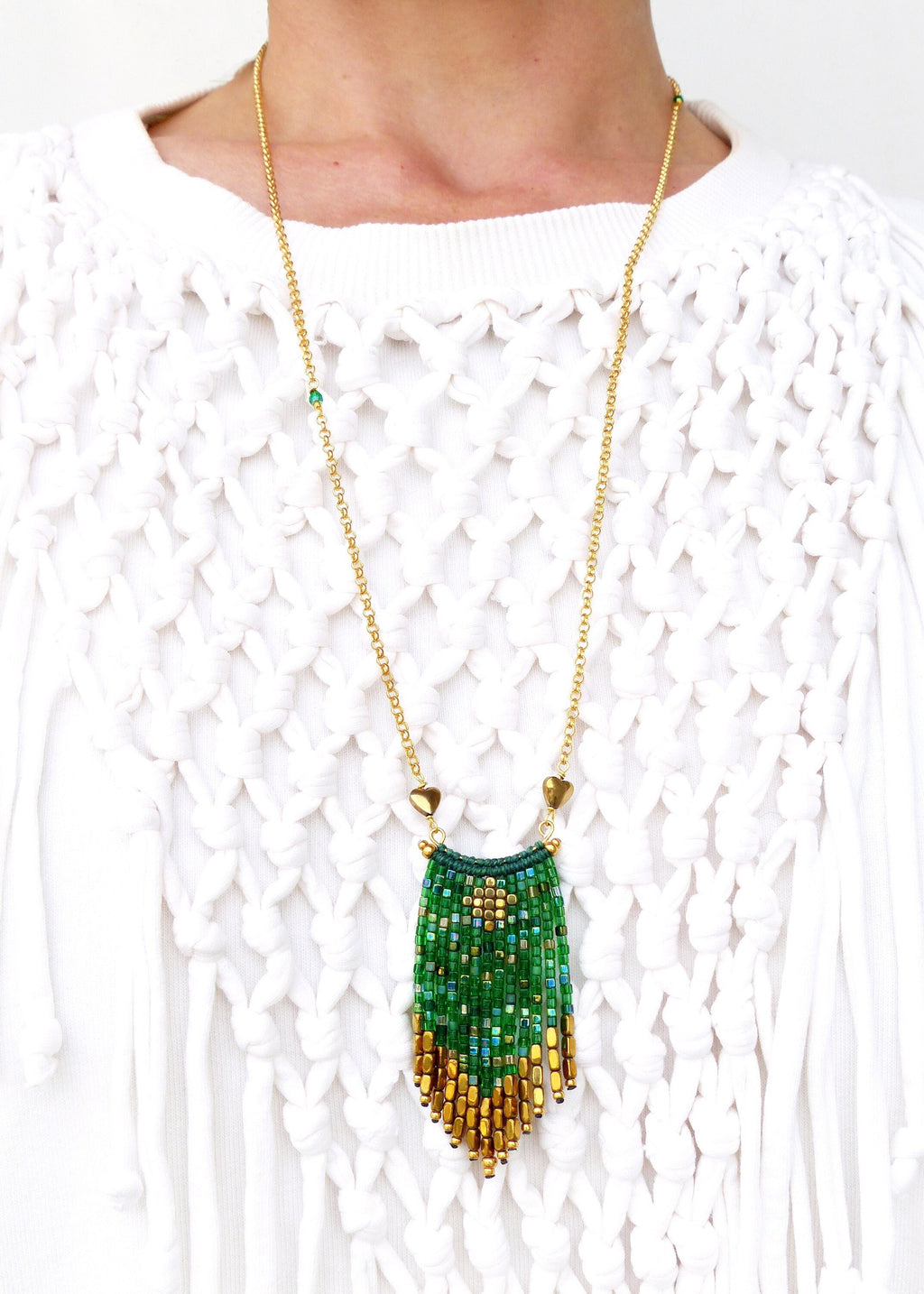 Peut inclure: Un collier en chaîne dorée avec un pendentif en perles vertes et dorées. Le pendentif a la forme d'une larme et est orné d'une frange de perles dorées.