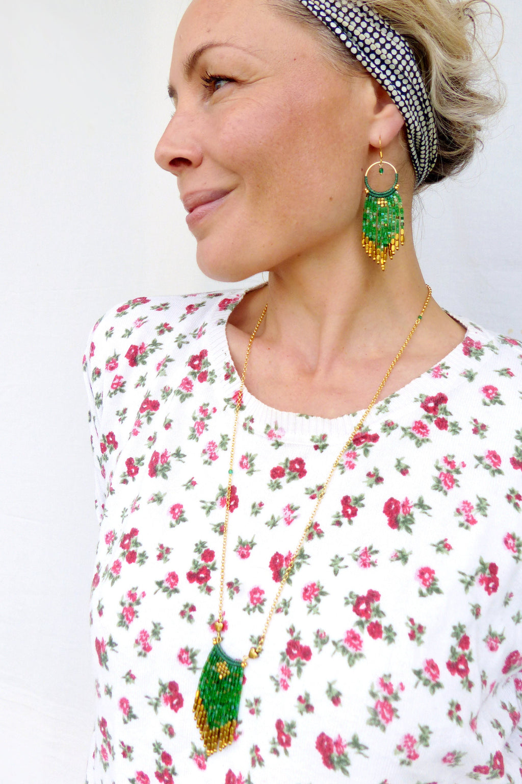 Peut inclure: Une femme portant une chemise blanche à fleurs avec un collier en chaîne dorée et des boucles d'oreilles en perles vertes et dorées. Le collier et les boucles d'oreilles ont une forme de larme avec une frange de perles.