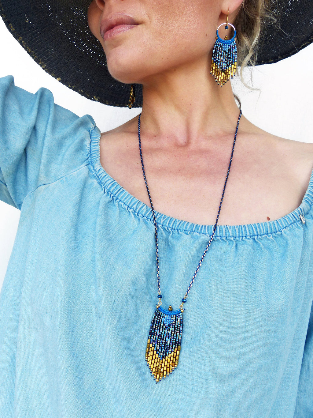 Peut inclure: Un collier et des boucles d'oreilles en perles bleues et dorées. Le collier a un pendentif en forme de larme avec un accent doré en haut. Les boucles d'oreilles sont longues et pendantes, avec un anneau doré en haut.