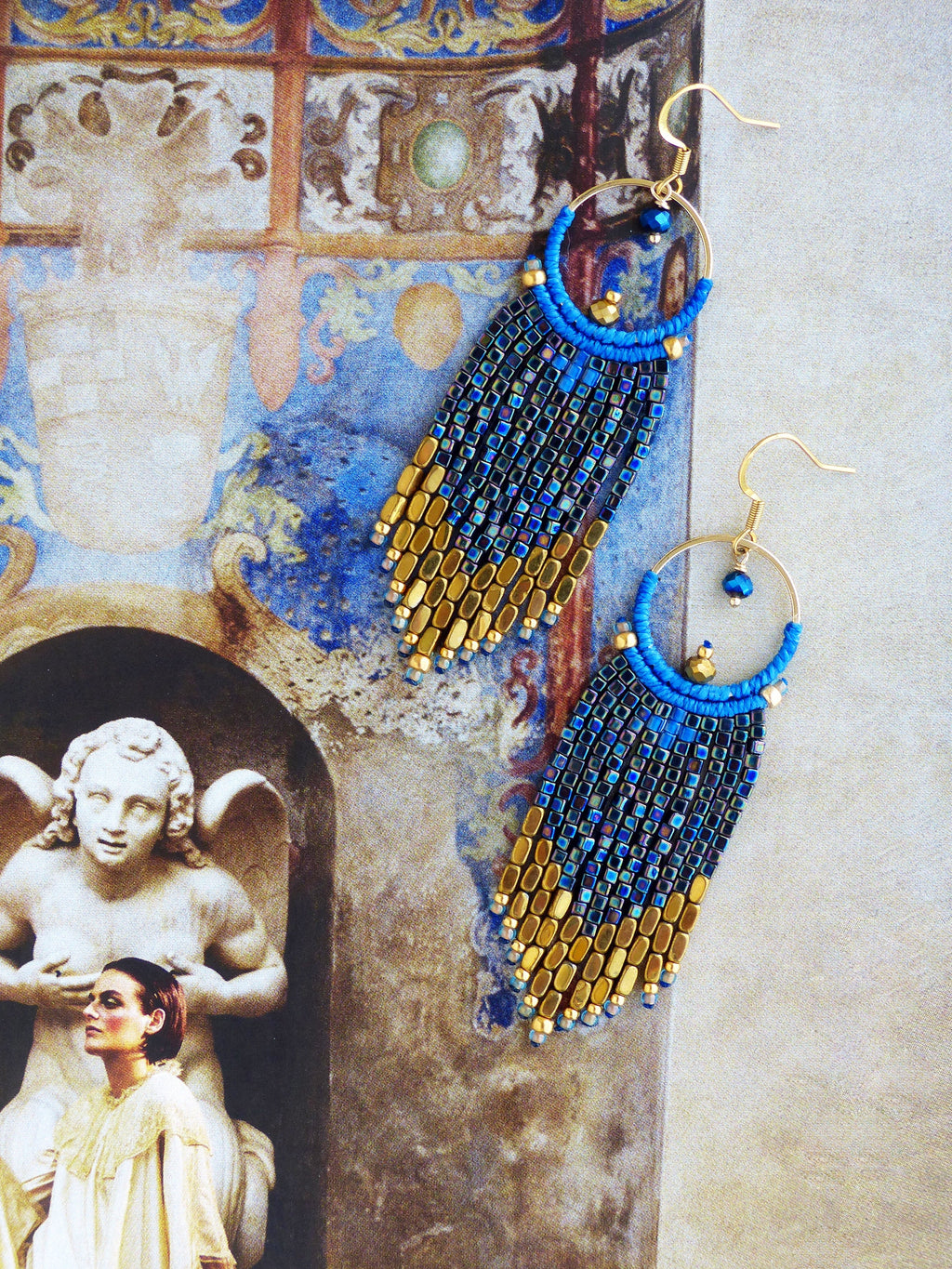 Peut inclure: Boucles d'oreilles faites à la main, bleues et dorées. Elles présentent un cercle supérieur et une frange de petites perles rectangulaires, passant du bleu à l'or. Les boucles d'oreilles ont des crochets d'oreilles dorés.