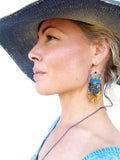Peut inclure: Une femme porte un chapeau de soleil bleu et un haut bleu. Elle porte des boucles d'oreilles à franges dorées et bleues. Un collier bleu est également visible. Le fond est blanc.