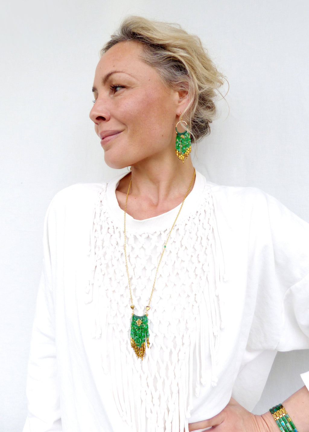Peut inclure: Une femme portant une chemise blanche avec un collier en chaîne dorée et des boucles d'oreilles en perles vertes et dorées. Le collier et les boucles d'oreilles présentent un design en frange.