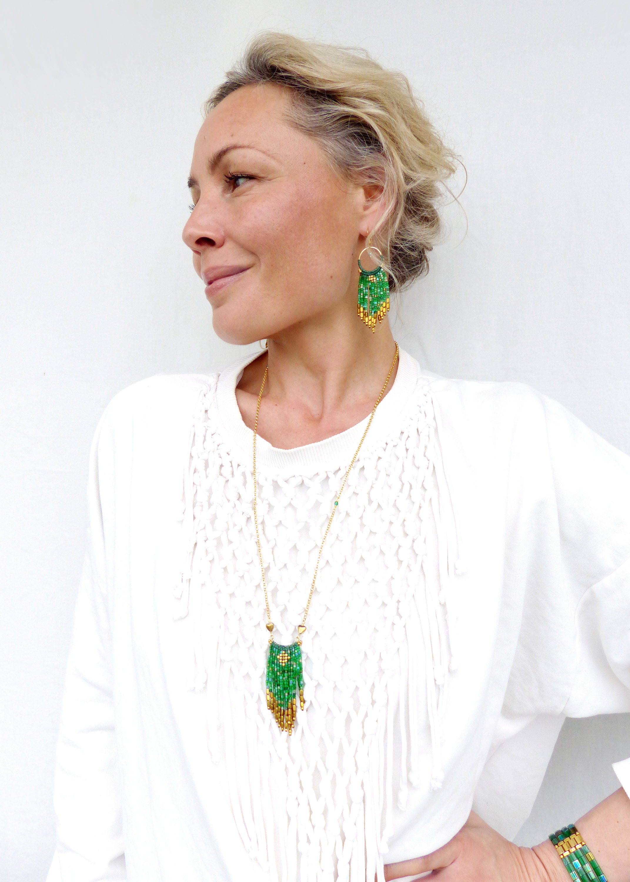 Peut inclure: Une femme portant une chemise blanche avec un collier en chaîne dorée et des boucles d'oreilles en perles vertes et dorées. Le collier et les boucles d'oreilles présentent un design en frange.