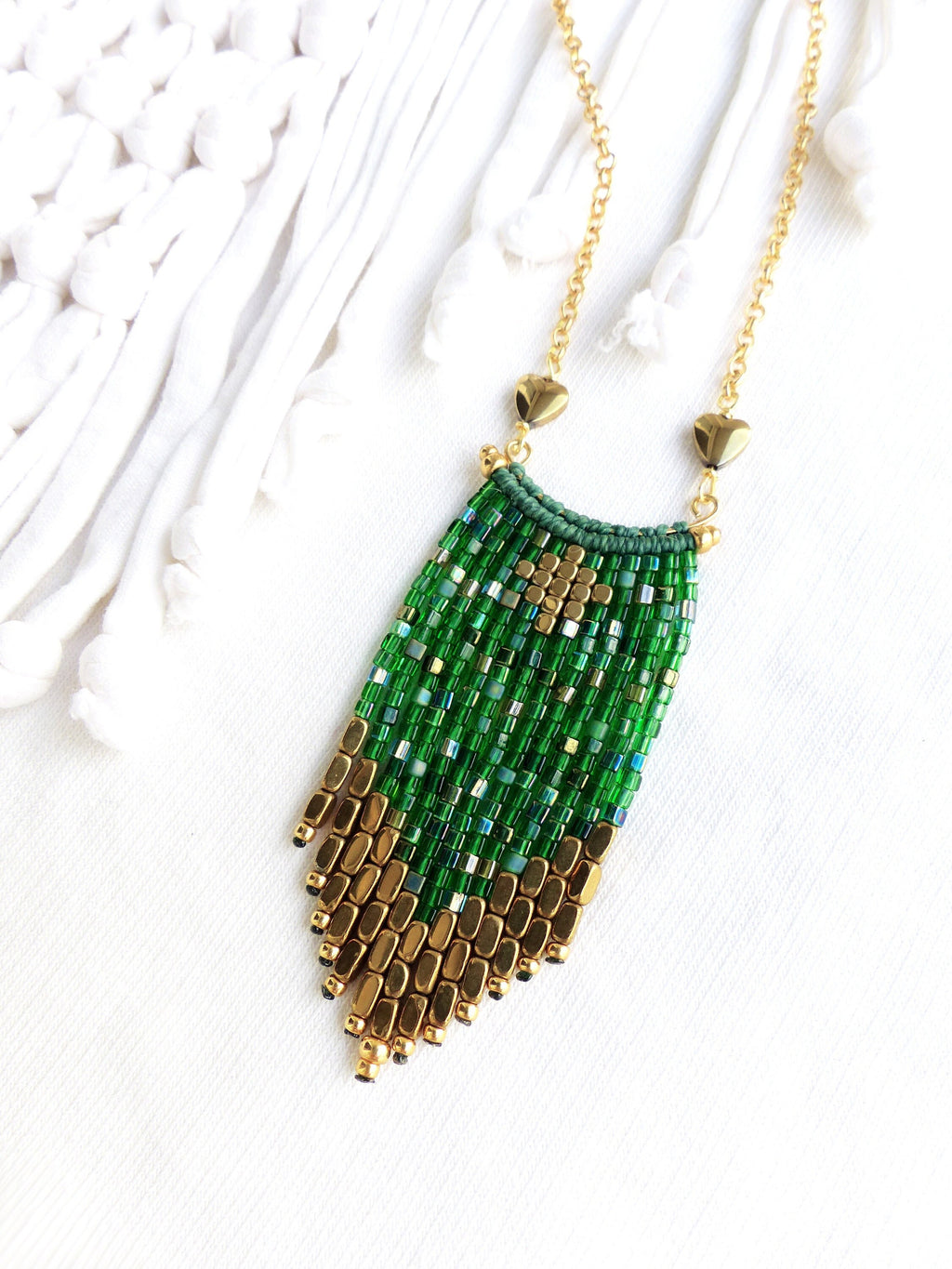 Peut inclure: Un collier en chaîne dorée avec un pendentif en perles vertes et dorées. Le pendentif est un long rectangle étroit avec un motif géométrique. Les perles sont petites et serrées.