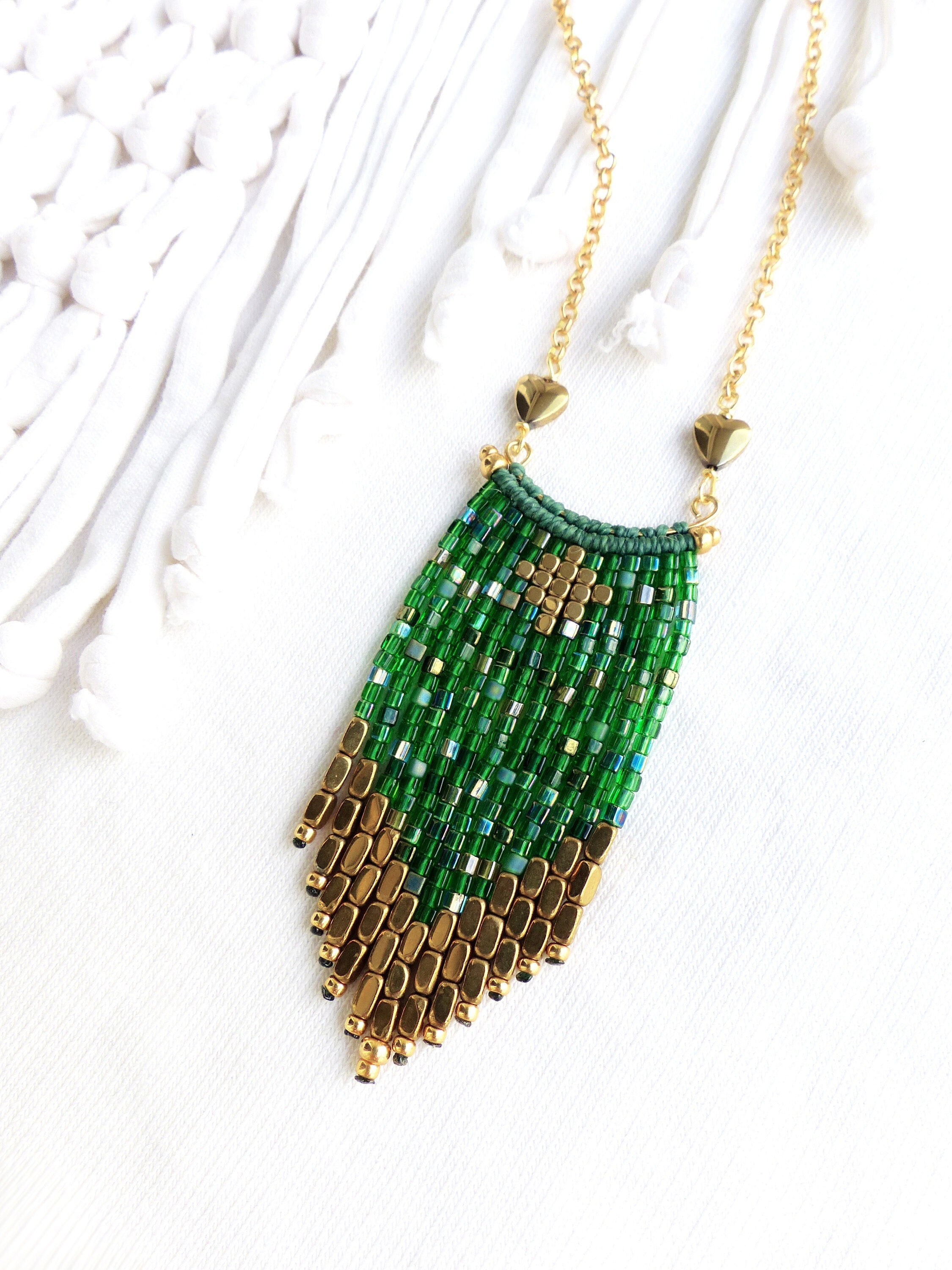 Peut inclure: Un collier en chaîne dorée avec un pendentif en perles vertes et dorées. Le pendentif est un long rectangle étroit avec un motif géométrique. Les perles sont petites et serrées.