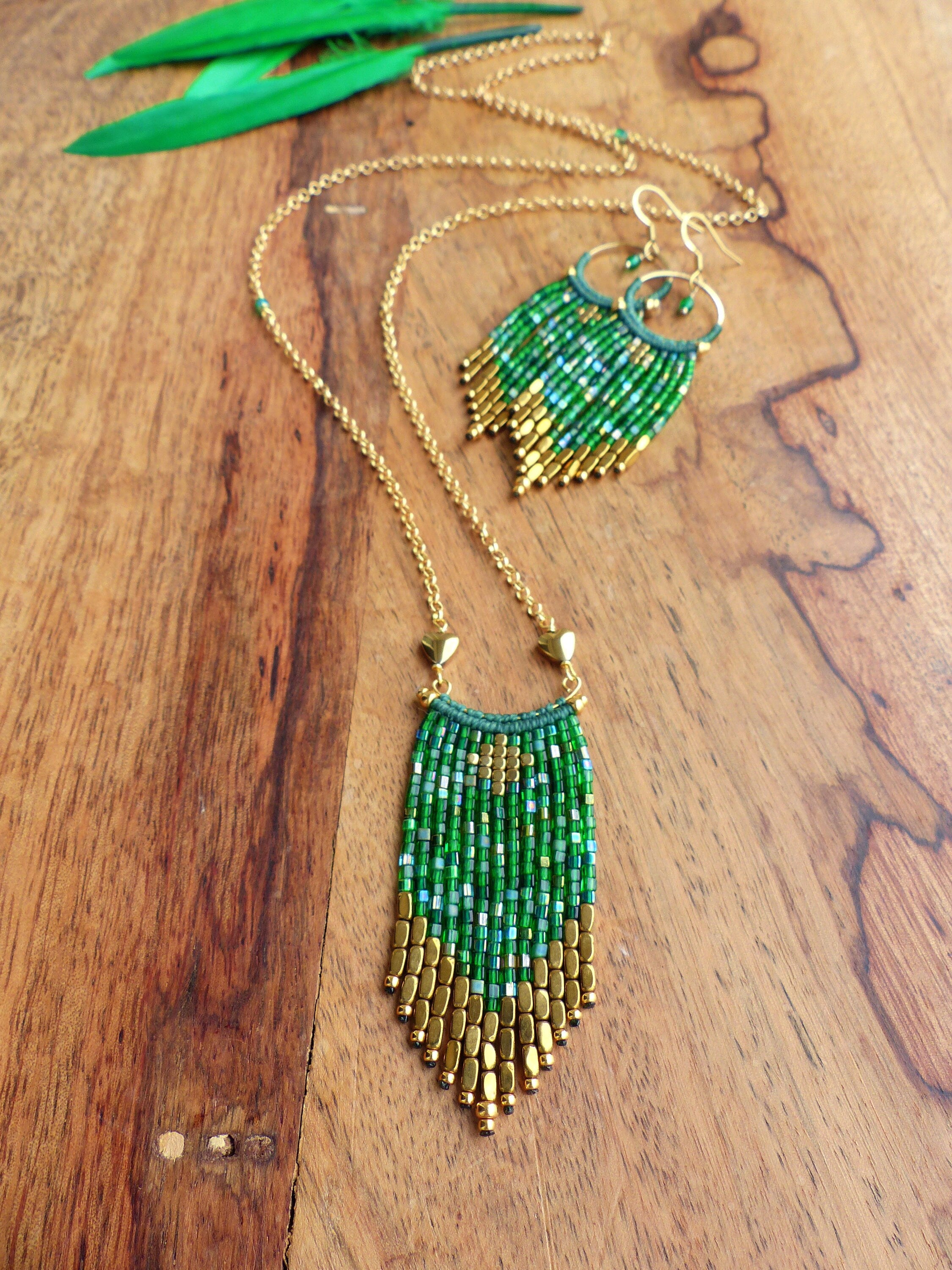 Peut inclure: Un collier et des boucles d'oreilles assortis en chaîne dorée avec des franges de perles vertes et dorées. Le collier et les boucles d'oreilles sont sur une surface en bois.