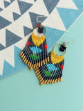 Peut inclure: Une paire de longues boucles d'oreilles en perles avec un pendentif en forme de flèche noire. Les boucles d'oreilles sont faites de perles noires, dorées, jaunes, bleues, vertes et rouges.