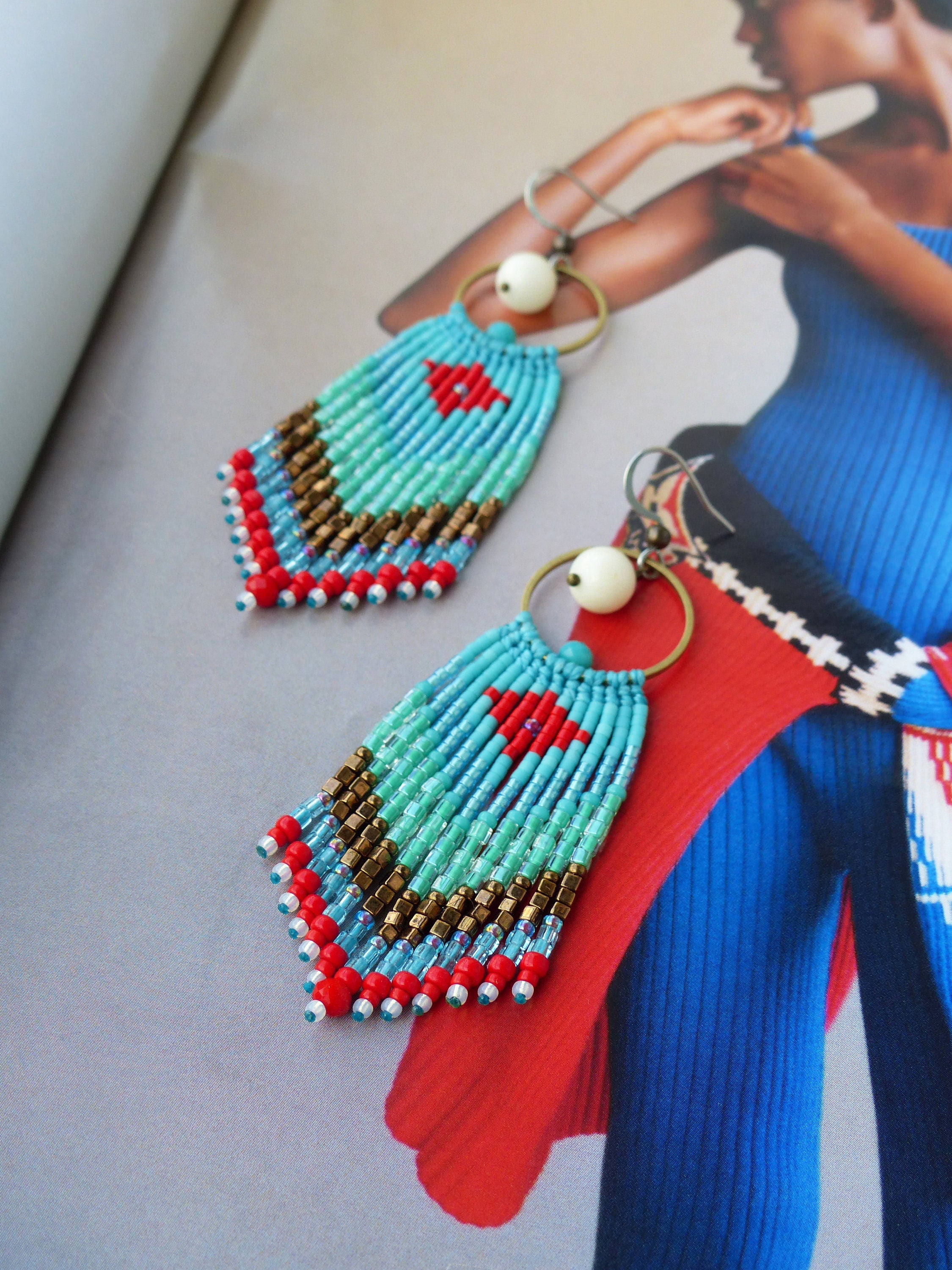 Peut inclure: Une paire de boucles d'oreilles en perles turquoise et rouge avec une perle blanche et un anneau doré. Les boucles d'oreilles sont faites à la main et présentent un design en frange.