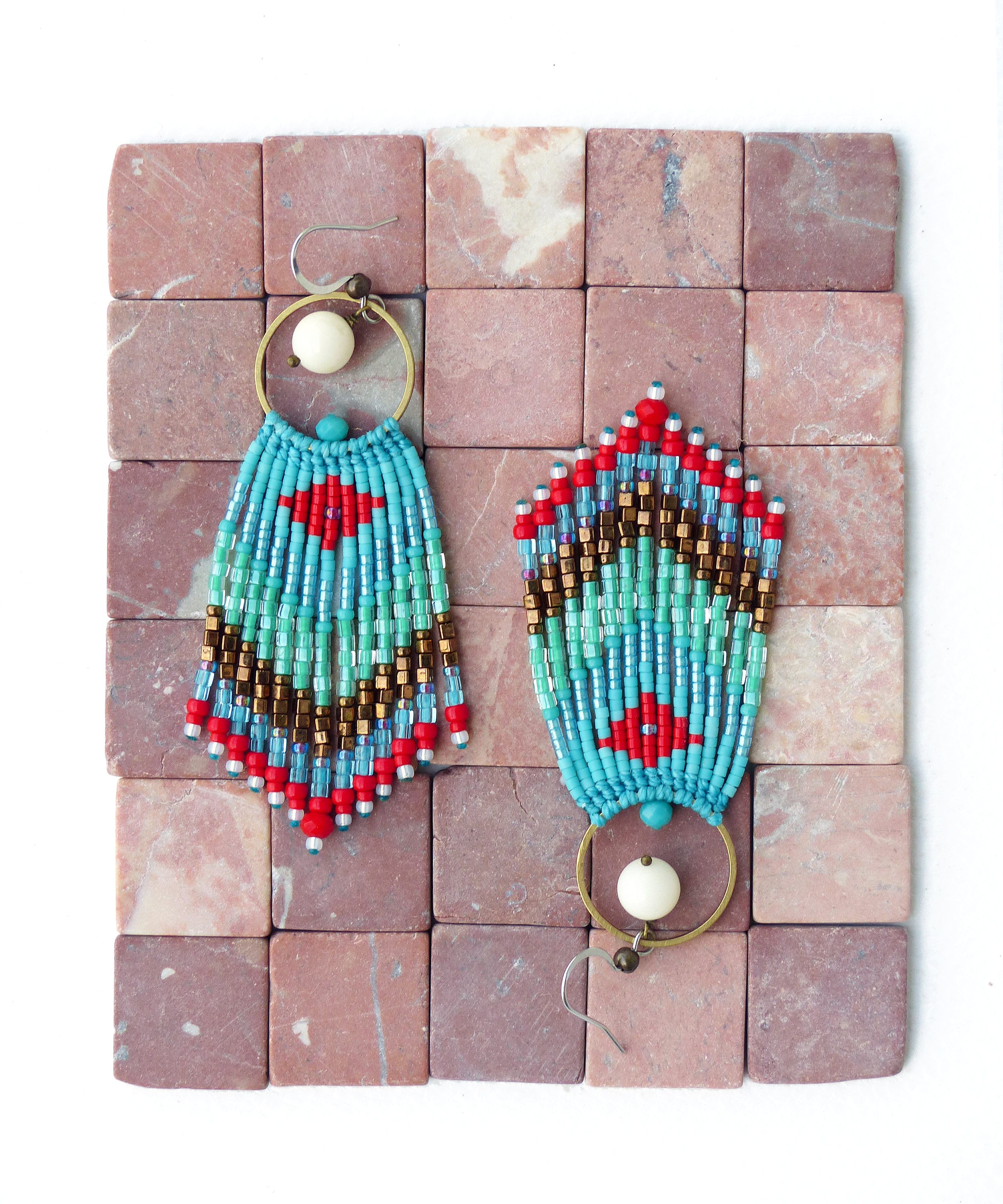 Peut inclure: Une paire de boucles d'oreilles pendantes en perles turquoise, rouge et or avec une perle blanche au sommet de chaque boucle d'oreille.