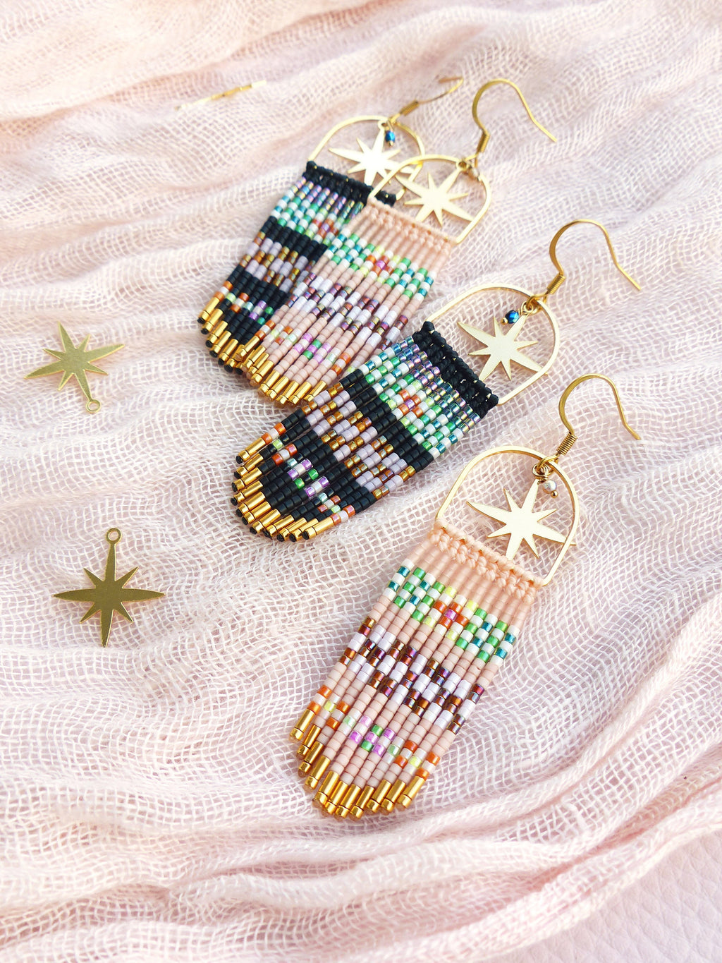 Peut inclure: Une paire de longues boucles d'oreilles en perles avec des breloques en forme d'étoile dorée. Les boucles d'oreilles sont faites avec une variété de perles colorées, dont du rose, du noir, du blanc et du vert. 