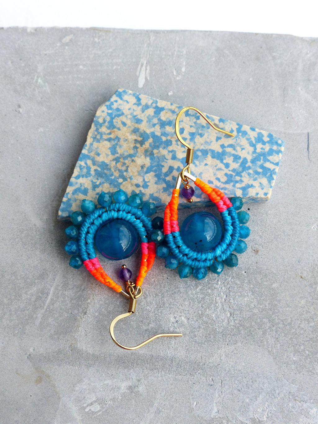 Peut inclure: Une paire de boucles d'oreilles en turquoise et bleu avec du fil orange et rose enroulé autour des pierres. Les boucles d'oreilles ont des crochets dorés.