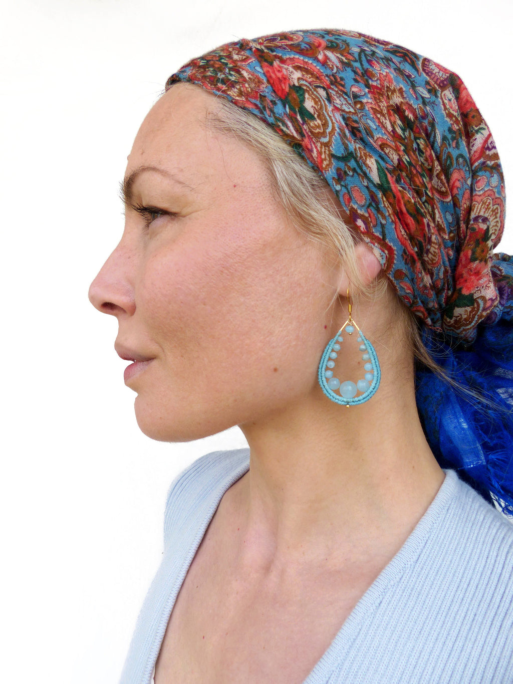 Peut inclure: Une femme portant un foulard à motifs bleus et rouges avec une paire de boucles d'oreilles turquoise en forme de larme. Les boucles d'oreilles sont faites de petites perles turquoise et de fil d'or.