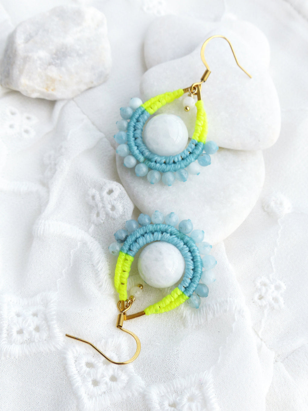 Peut inclure: Une paire de boucles d'oreilles pendantes avec un design en macramé bleu clair et jaune fluo. Les boucles d'oreilles présentent une pierre blanche au centre de chaque design.