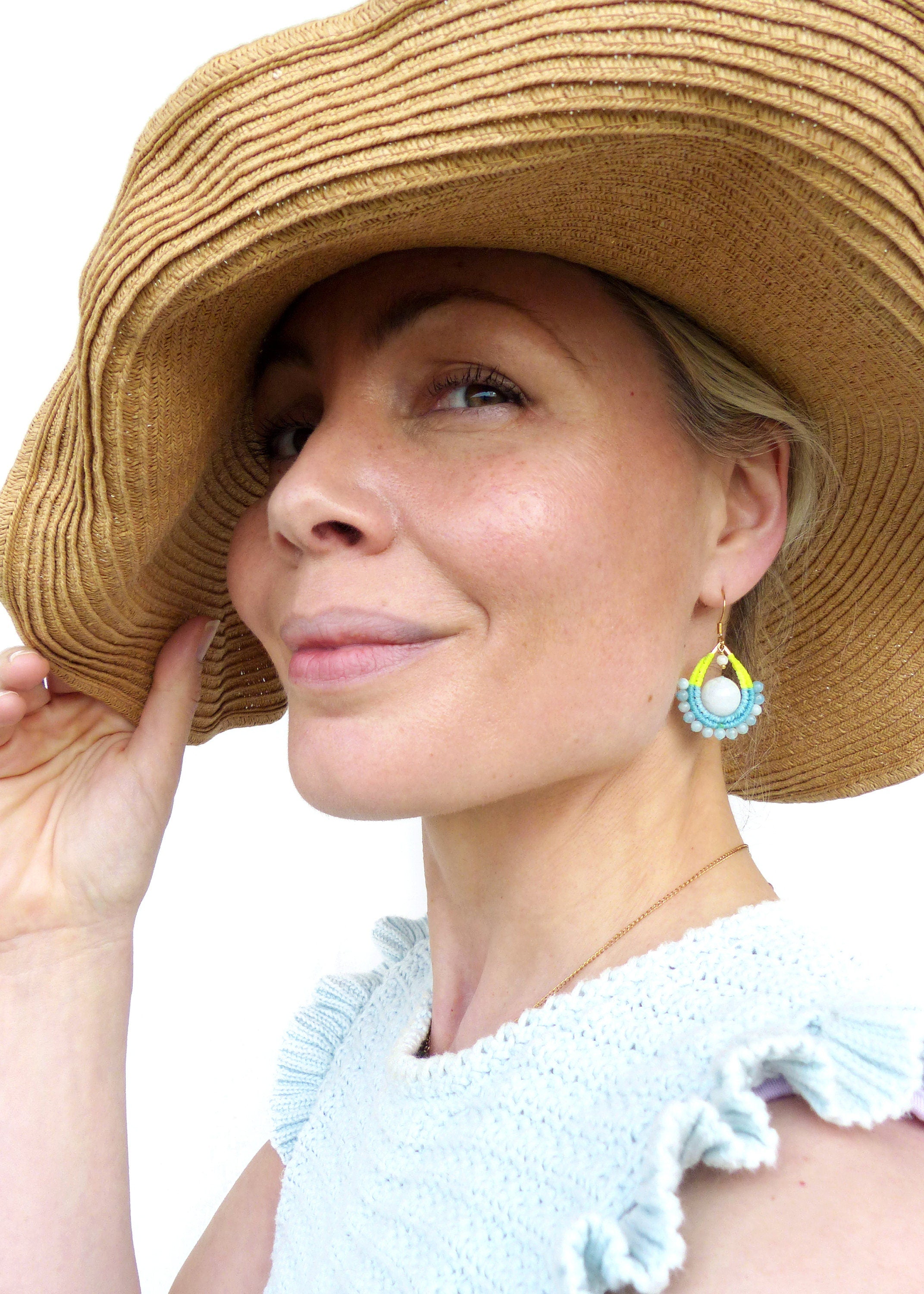 Peut inclure: Une femme portant un chapeau de paille et un haut bleu clair à col volanté. Elle porte une paire de boucles d'oreilles pendantes avec une perle blanche et des perles bleues et jaunes.