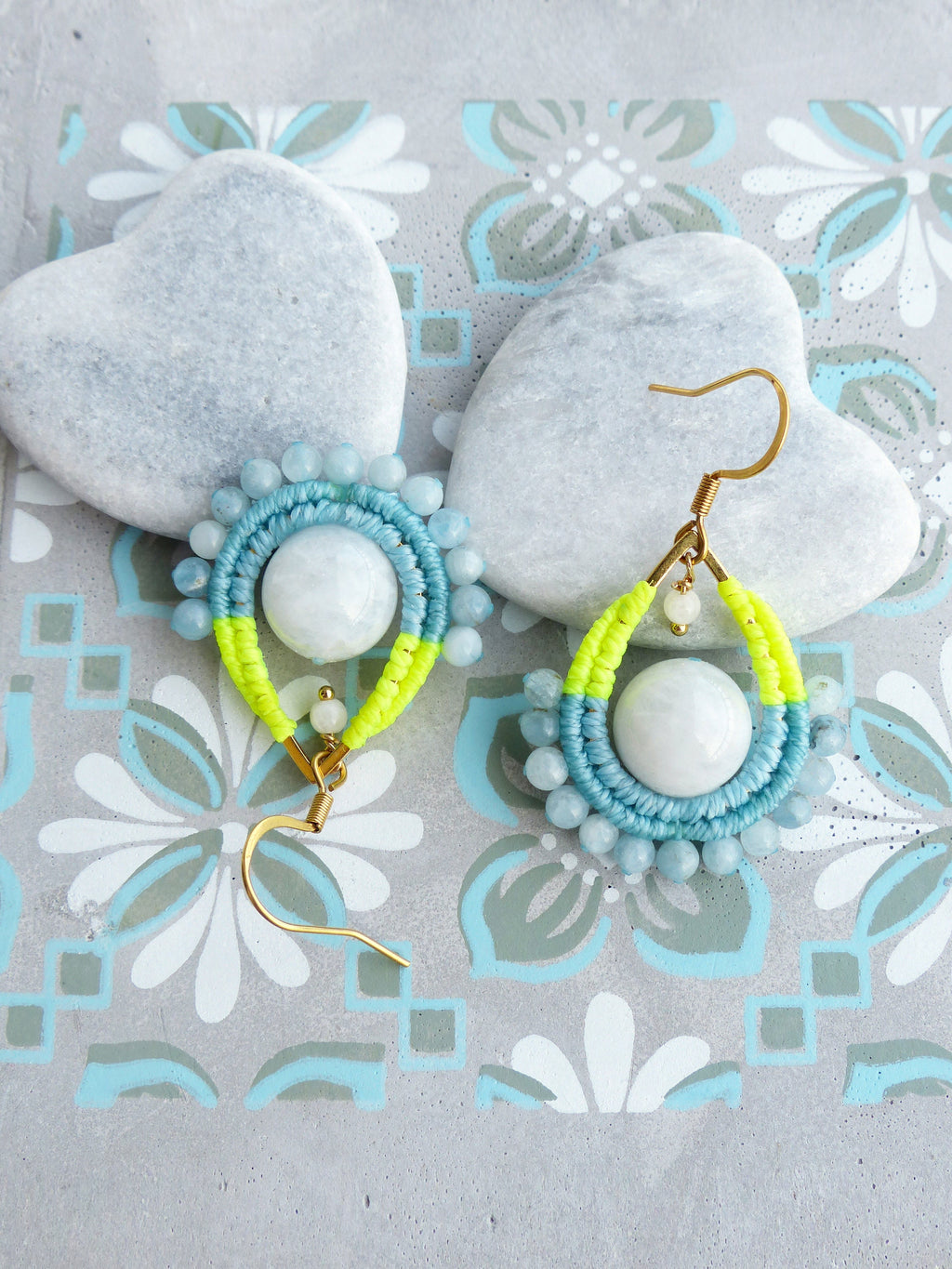 Peut inclure: Une paire de boucles d'oreilles avec un centre en pierre blanche, entouré de perles bleues et vertes. Les boucles d'oreilles sont suspendues à des crochets dorés.
