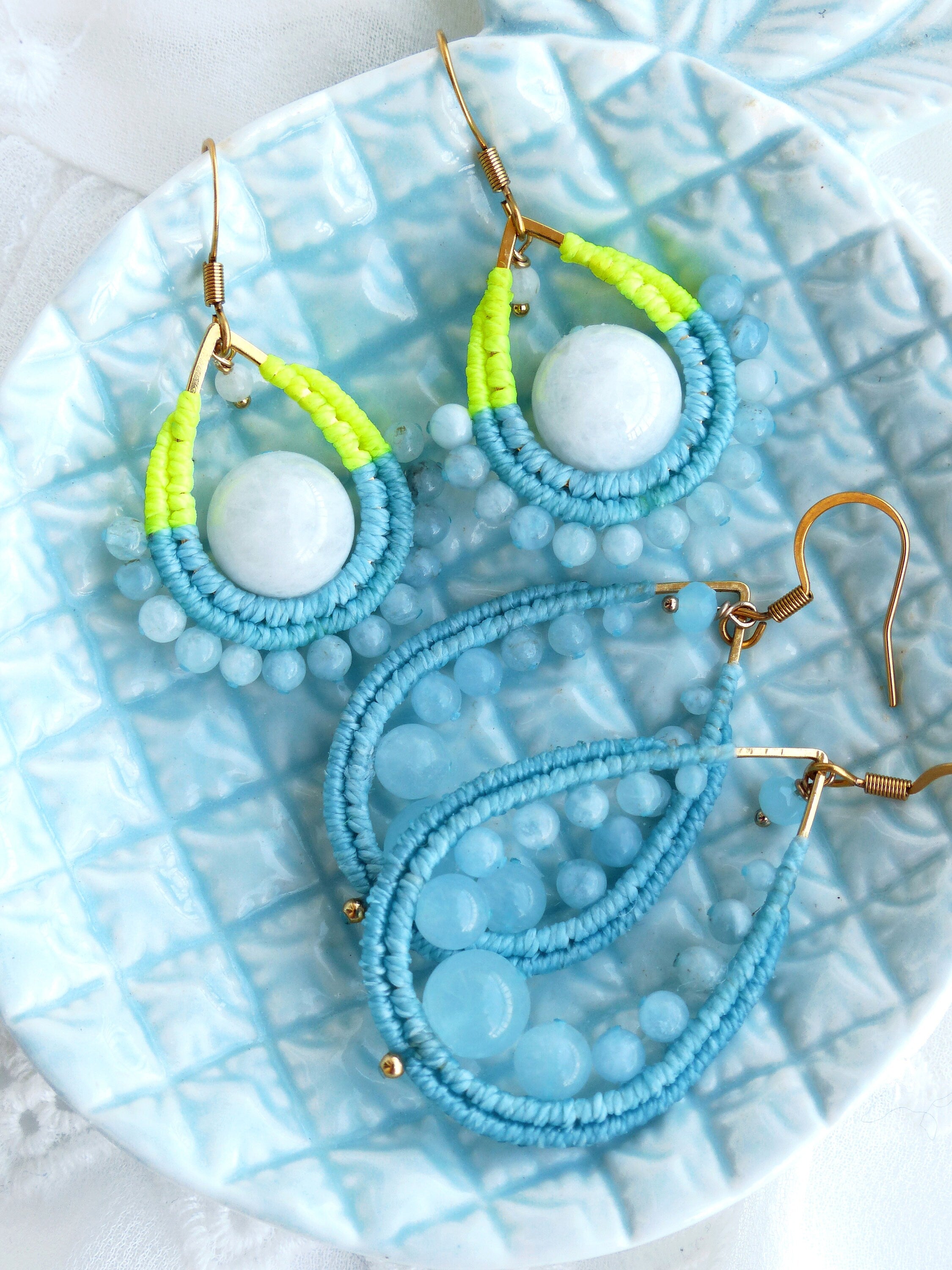 Peut inclure: Une paire de boucles d'oreilles en perles bleues et vert néon avec un pendentif en pierre précieuse bleu clair. Les boucles d'oreilles sont sur un fond bleu clair.