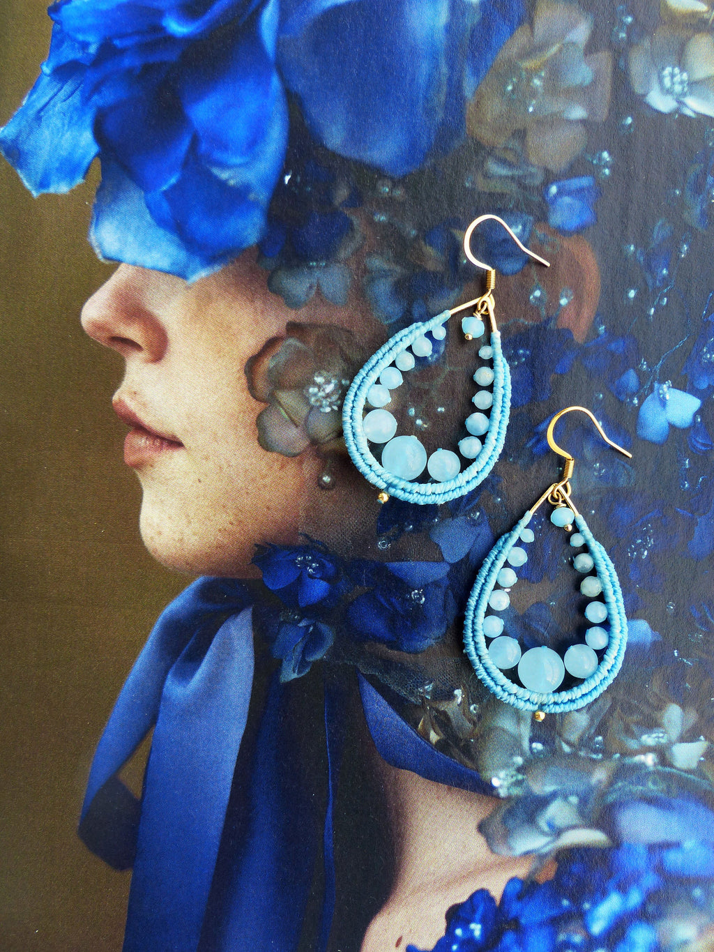 Peut inclure: Une paire de boucles d'oreilles en forme de larme avec des perles bleues et des accents dorés. Les boucles d'oreilles pendent de l'oreille d'un mannequin.