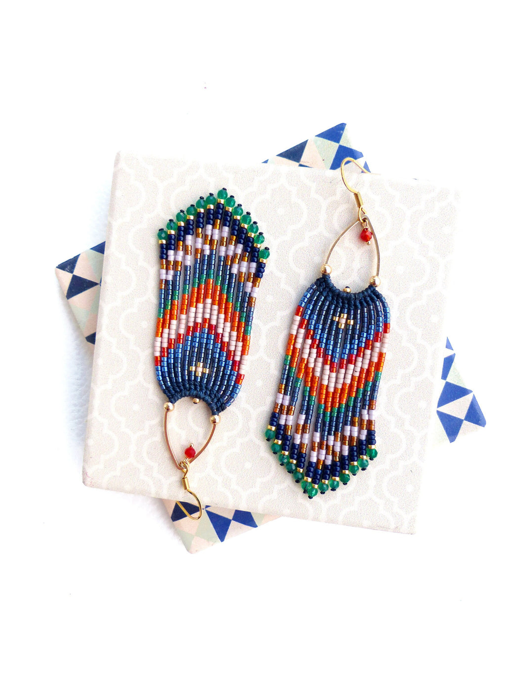 Peut inclure: Une paire de boucles d'oreilles perlées faites à la main avec un design à franges. Les boucles d'oreilles présentent une combinaison de perles bleues, orange, vertes et blanches. Les boucles d'oreilles ont des crochets dorés et de petites perles rouges.