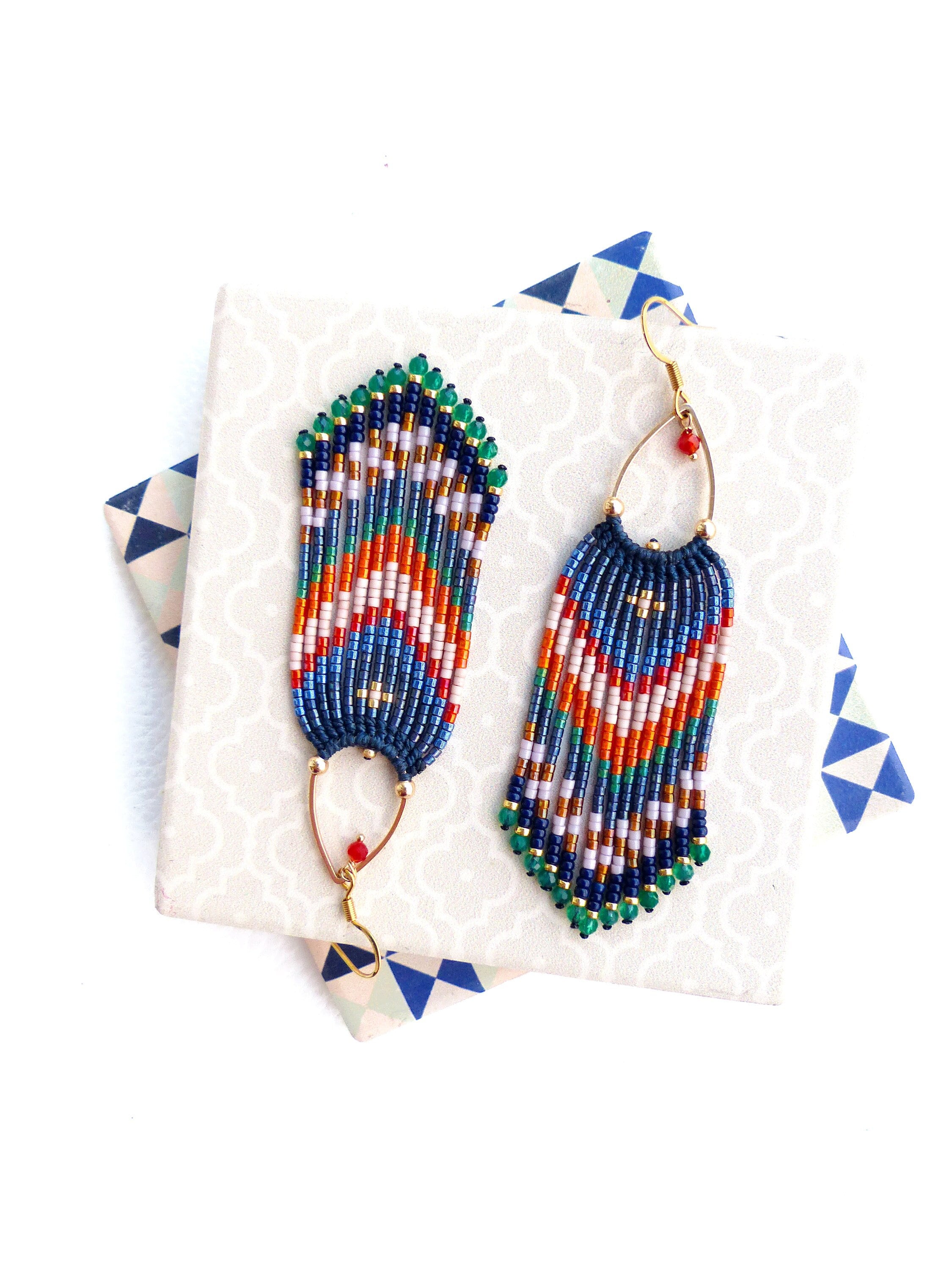 Peut inclure: Une paire de boucles d'oreilles perlées faites à la main avec un design à franges. Les boucles d'oreilles présentent une combinaison de perles bleues, orange, vertes et blanches. Les boucles d'oreilles ont des crochets dorés et de petites perles rouges.